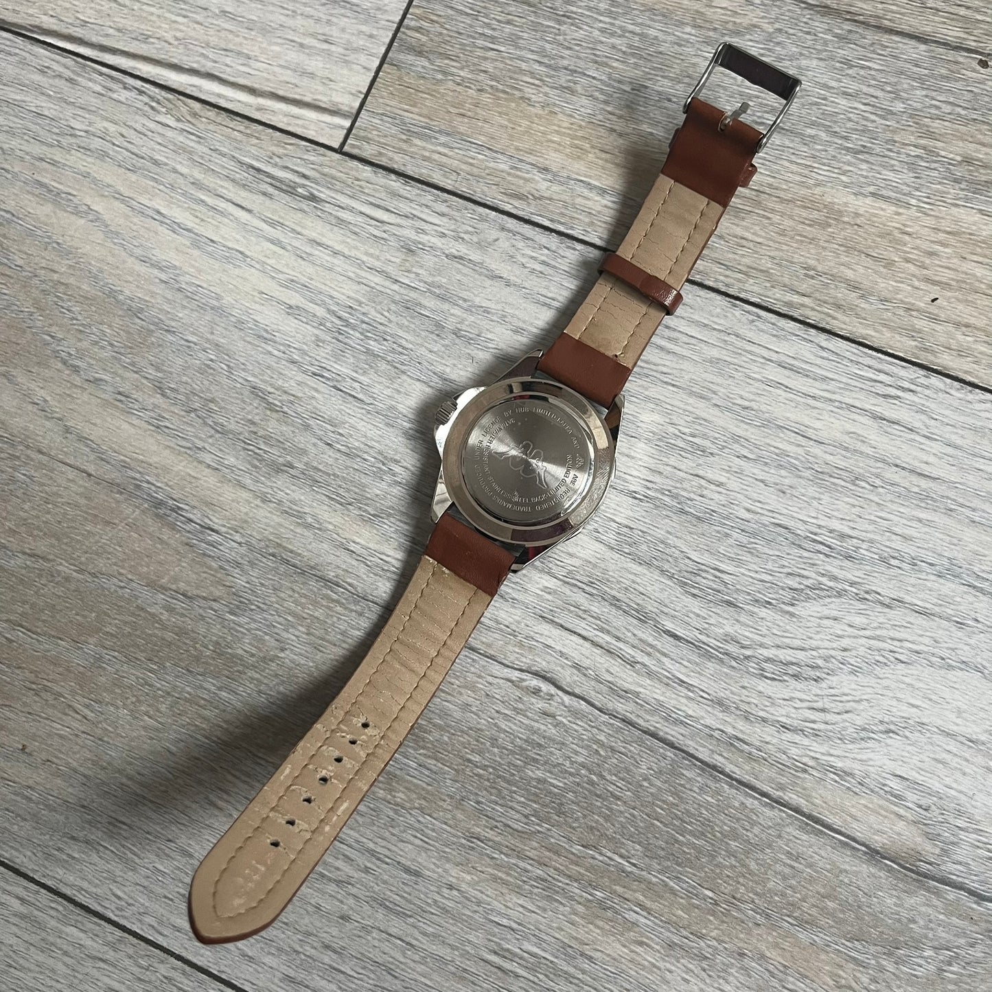 Kappa 2000s Quartz Analog Watch features brown leather straps, a silver-tone case, and a white dial. The bezel is marked in five-minute increments from 5 to 55. The dial has a Kappa logo at the top and Kappa text below the center. The hour markers are represented by white dots and numerals. The watch has a stainless steel case back and is marked as a limited edition model.
