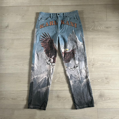 The Karl Kani Signature Eagle Printed Jeans feature a multi-tone eagle graphic over a mountain landscape on a classic blue denim base. Made from 100% cotton, these baggy jeans have a relaxed, wide-leg fit with straight cut legs, a button and zip fastening, and embroidered Karl Kani branding on the back and front pockets. The all-over print extends across the front and back, creating a unique and vintage-inspired look from the FW22 Season.