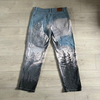 The Karl Kani Signature Eagle Printed Jeans feature a multi-tone eagle graphic over a mountain landscape on a classic blue denim base. Made from 100% cotton, these baggy jeans have a relaxed, wide-leg fit with straight cut legs, a button and zip fastening, and embroidered Karl Kani branding on the back and front pockets. The all-over print extends across the front and back, creating a unique and vintage-inspired look from the FW22 Season.