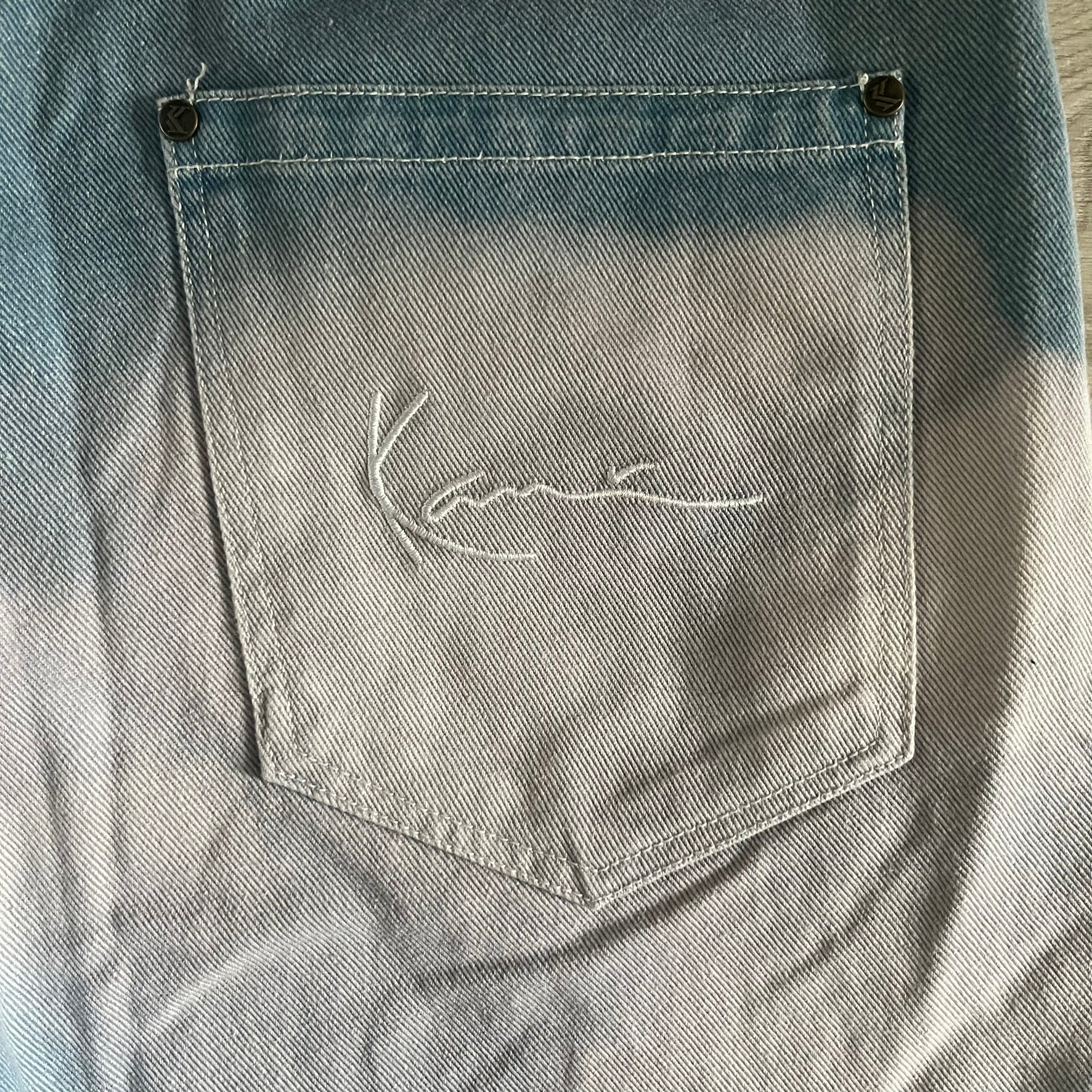 The Karl Kani Signature Eagle Printed Jeans feature a multi-tone eagle graphic over a mountain landscape on a classic blue denim base. Made from 100% cotton, these baggy jeans have a relaxed, wide-leg fit with straight cut legs, a button and zip fastening, and embroidered Karl Kani branding on the back and front pockets. The all-over print extends across the front and back, creating a unique and vintage-inspired look from the FW22 Season.