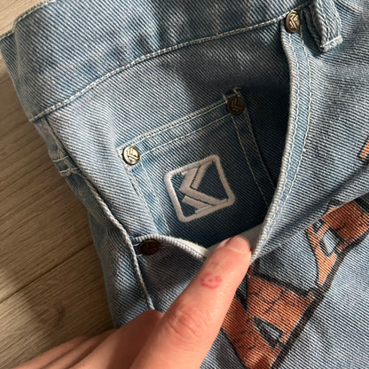 The Karl Kani Signature Eagle Printed Jeans feature a multi-tone eagle graphic over a mountain landscape on a classic blue denim base. Made from 100% cotton, these baggy jeans have a relaxed, wide-leg fit with straight cut legs, a button and zip fastening, and embroidered Karl Kani branding on the back and front pockets. The all-over print extends across the front and back, creating a unique and vintage-inspired look from the FW22 Season.