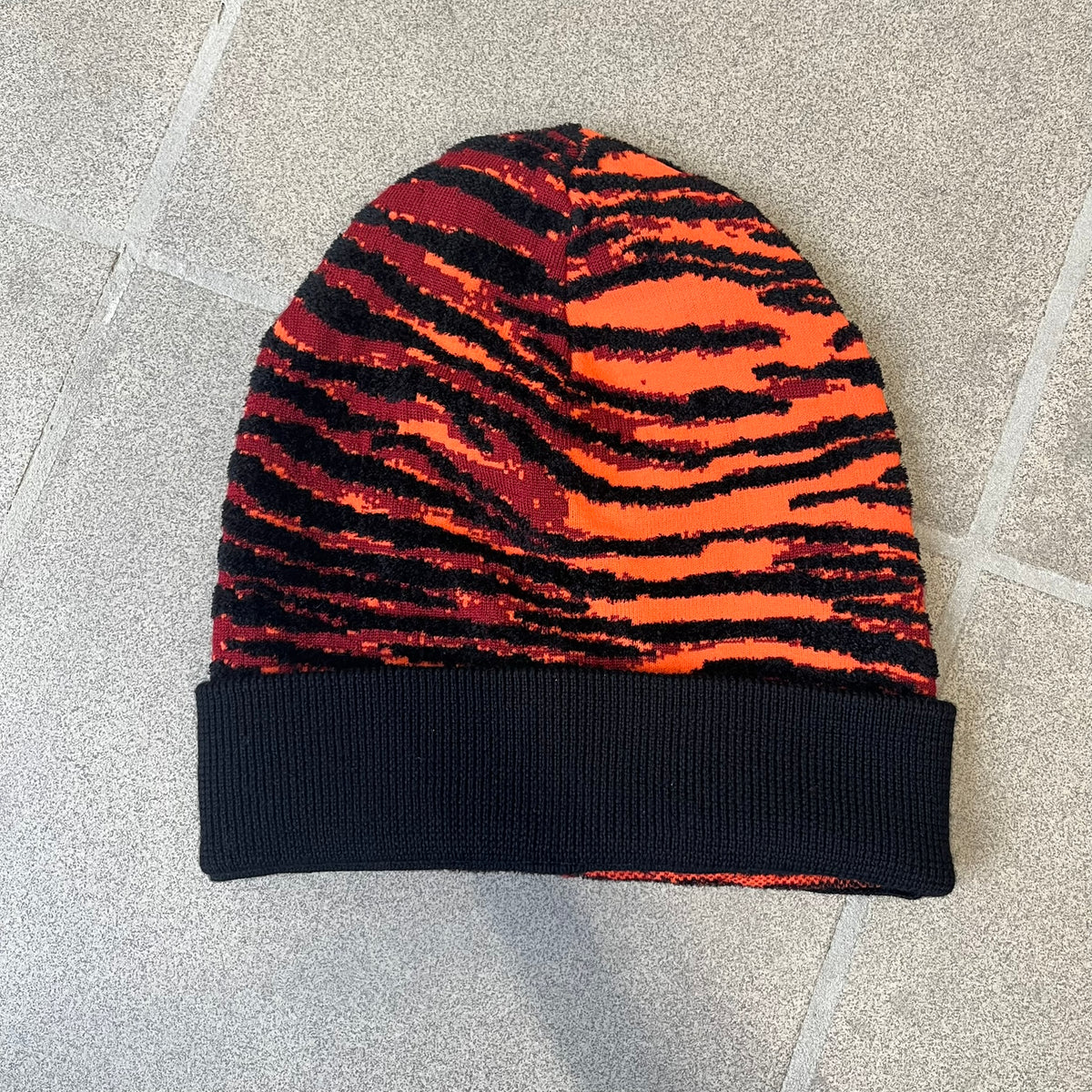 Kenzo x H&amp;M Orange Tiger Camo Beanie is a knit beanie from the 2016 collaboration. It features an all-over tiger camouflage pattern in red, orange, and dark red tones, woven directly into the fabric. The design is finished with a black cuff and can be worn either slouched or folded for a more traditional beanie fit.