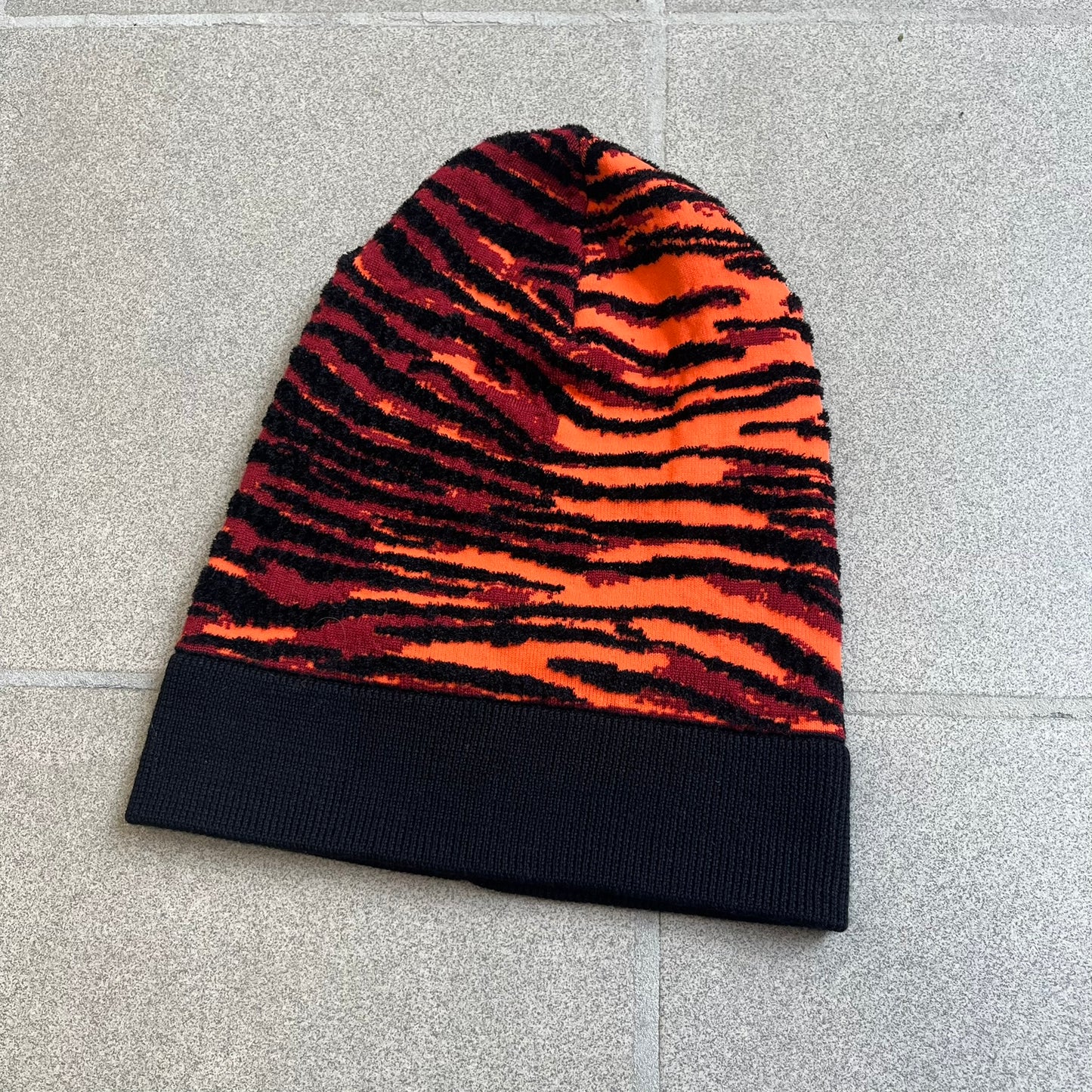 Kenzo x H&amp;M Orange Tiger Camo Beanie is a knit beanie from the 2016 collaboration. It features an all-over tiger camouflage pattern in red, orange, and dark red tones, woven directly into the fabric. The design is finished with a black cuff and can be worn either slouched or folded for a more traditional beanie fit.