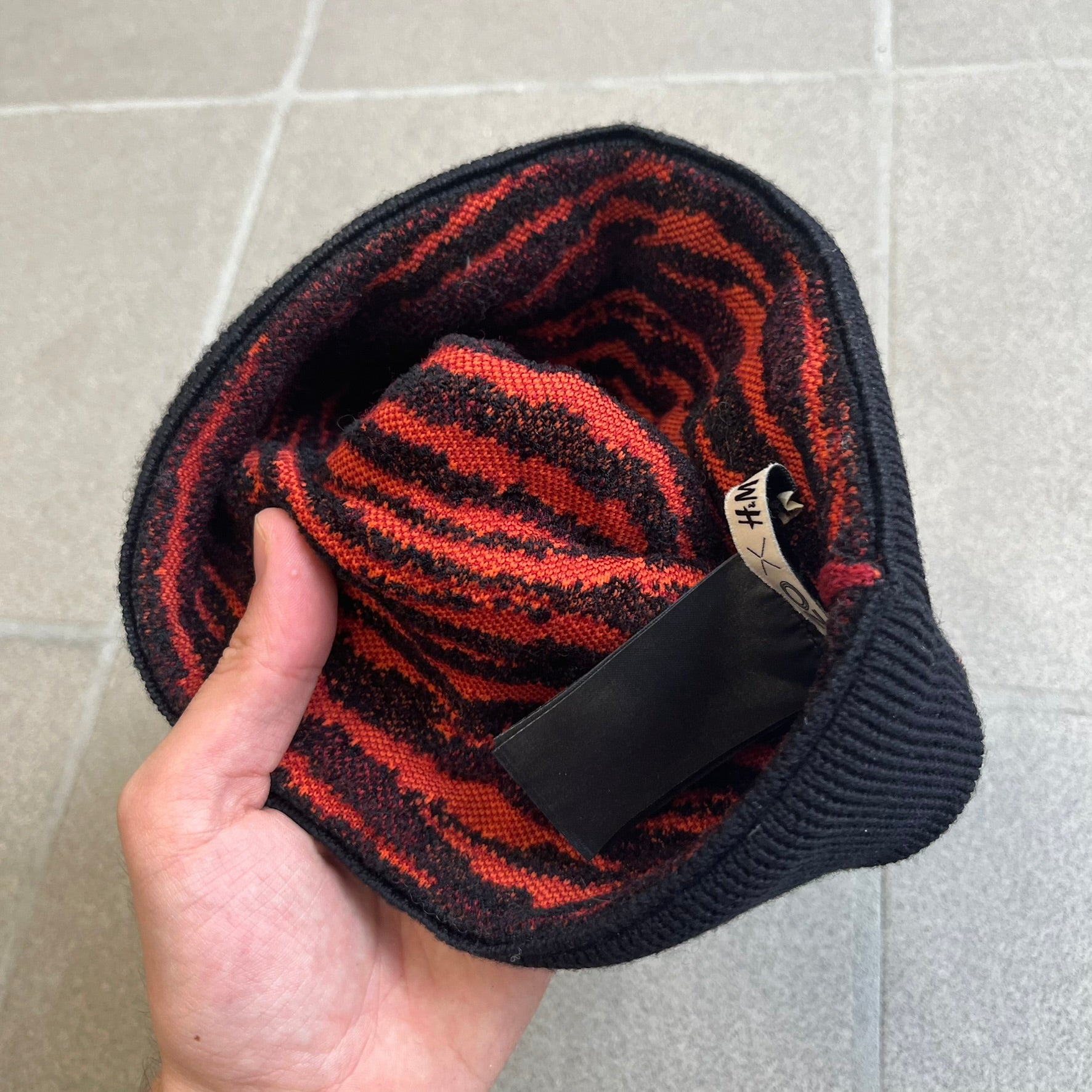 Kenzo x H&amp;M Orange Tiger Camo Beanie is a knit beanie from the 2016 collaboration. It features an all-over tiger camouflage pattern in red, orange, and dark red tones, woven directly into the fabric. The design is finished with a black cuff and can be worn either slouched or folded for a more traditional beanie fit.