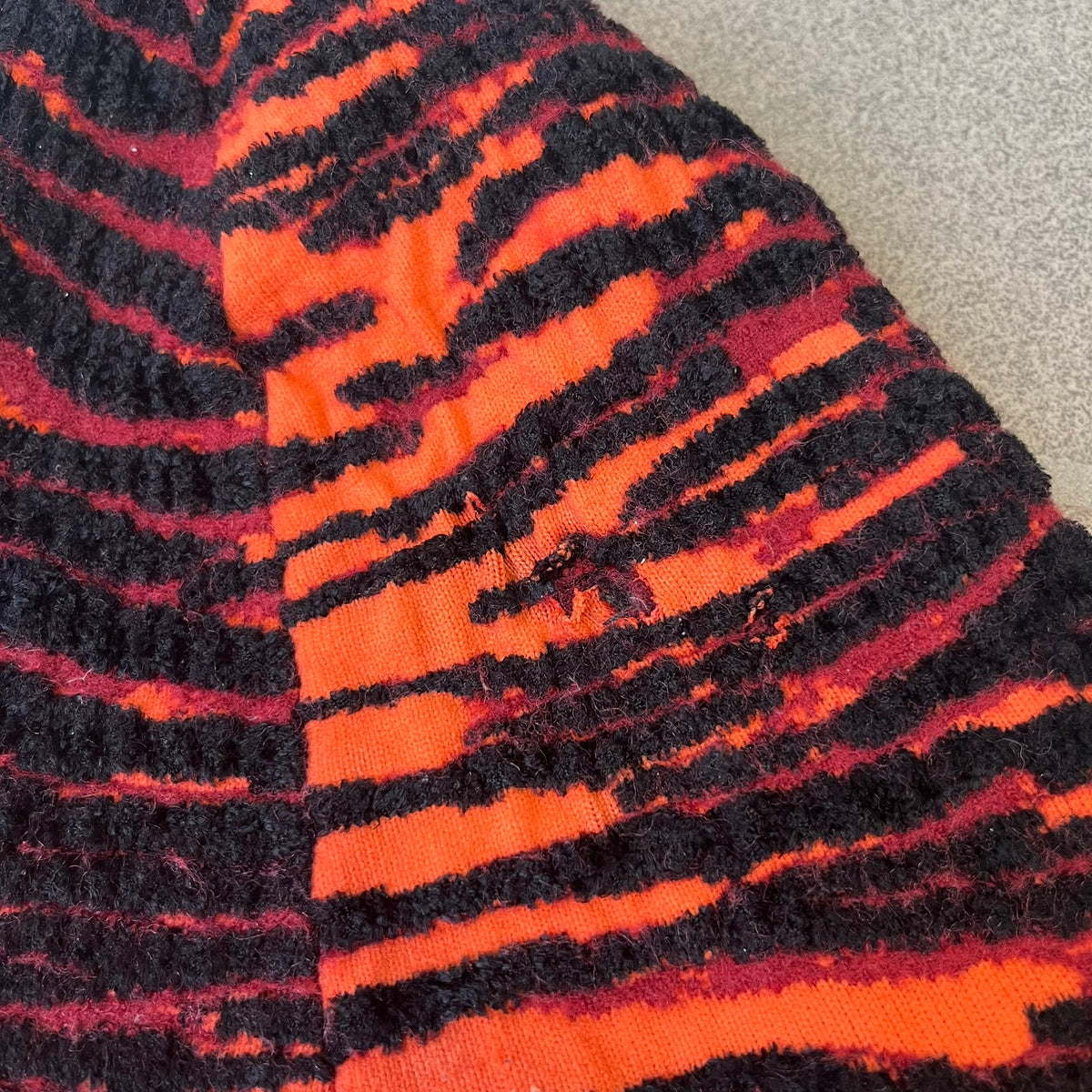 Kenzo x H&amp;M Orange Tiger Camo Beanie is a knit beanie from the 2016 collaboration. It features an all-over tiger camouflage pattern in red, orange, and dark red tones, woven directly into the fabric. This second version of the beanie is tighter and thicker, so the black cuff can't be folded.