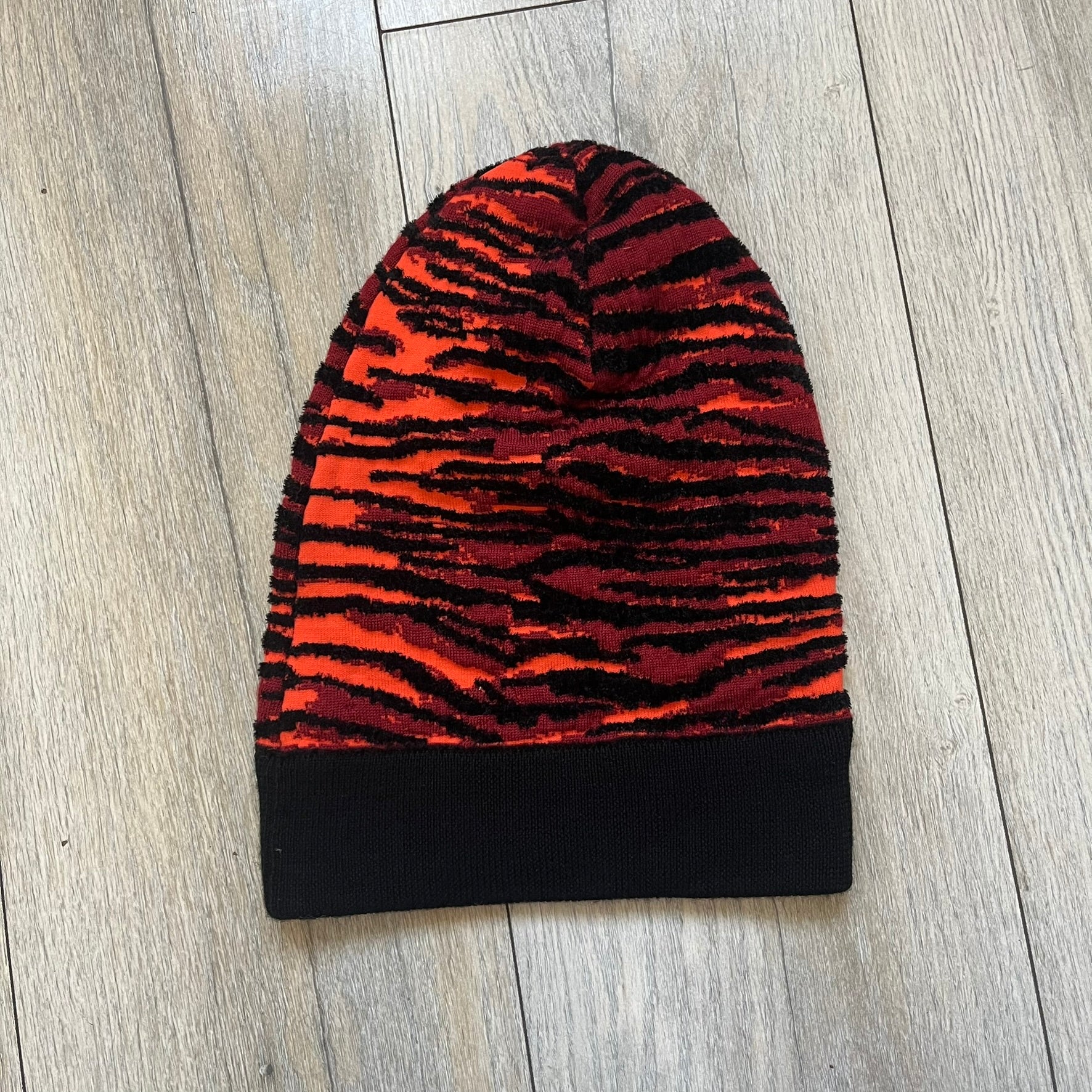 Kenzo x H&amp;M Orange Tiger Camo Beanie is a knit beanie from the 2016 collaboration. It features an all-over tiger camouflage pattern in red, orange, and dark red tones, woven directly into the fabric. The design is finished with a black cuff and can be worn either slouched or folded for a more traditional beanie fit.