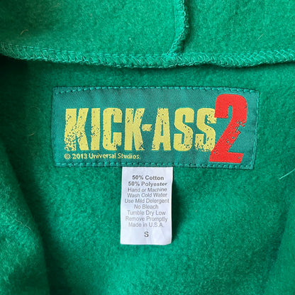 Kick-Ass 2 Full Zip 2013 Promo Hoodie is a green full-zip hoodie with yellow printed lines matching the costume worn by Kick-Ass in Kick-Ass 2. The zipper extends through the hood, allowing it to close into a mask with see-through mesh eye panels. It features a Kick-Ass 2 (2013) Universal Studios licensed neck tag, a matching movie logo patch on the sleeve, and is made in the USA.
