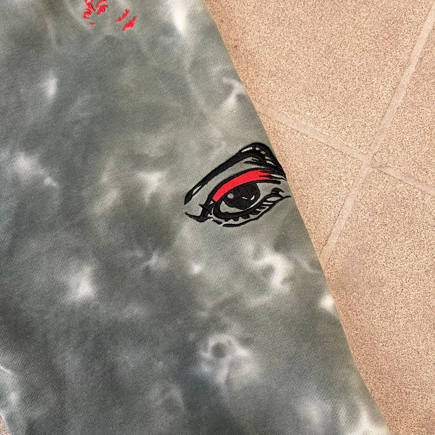 KidSuper Studios FW21 Tie-Dye Sweatpants feature a white and grey tie-dye colorway with multiple embroidered details throughout. The sweatpants include a blue KidSuper logo, eye graphics, “Resenha” text, text on the drawstrings, and additional embroidery on the back pockets. Finished with a pink size tag.