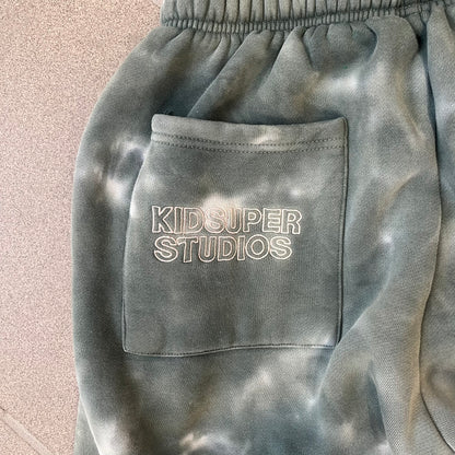 KidSuper Studios FW21 Tie-Dye Sweatpants feature a white and grey tie-dye colorway with multiple embroidered details throughout. The sweatpants include a blue KidSuper logo, eye graphics, “Resenha” text, text on the drawstrings, and additional embroidery on the back pockets. Finished with a pink size tag.