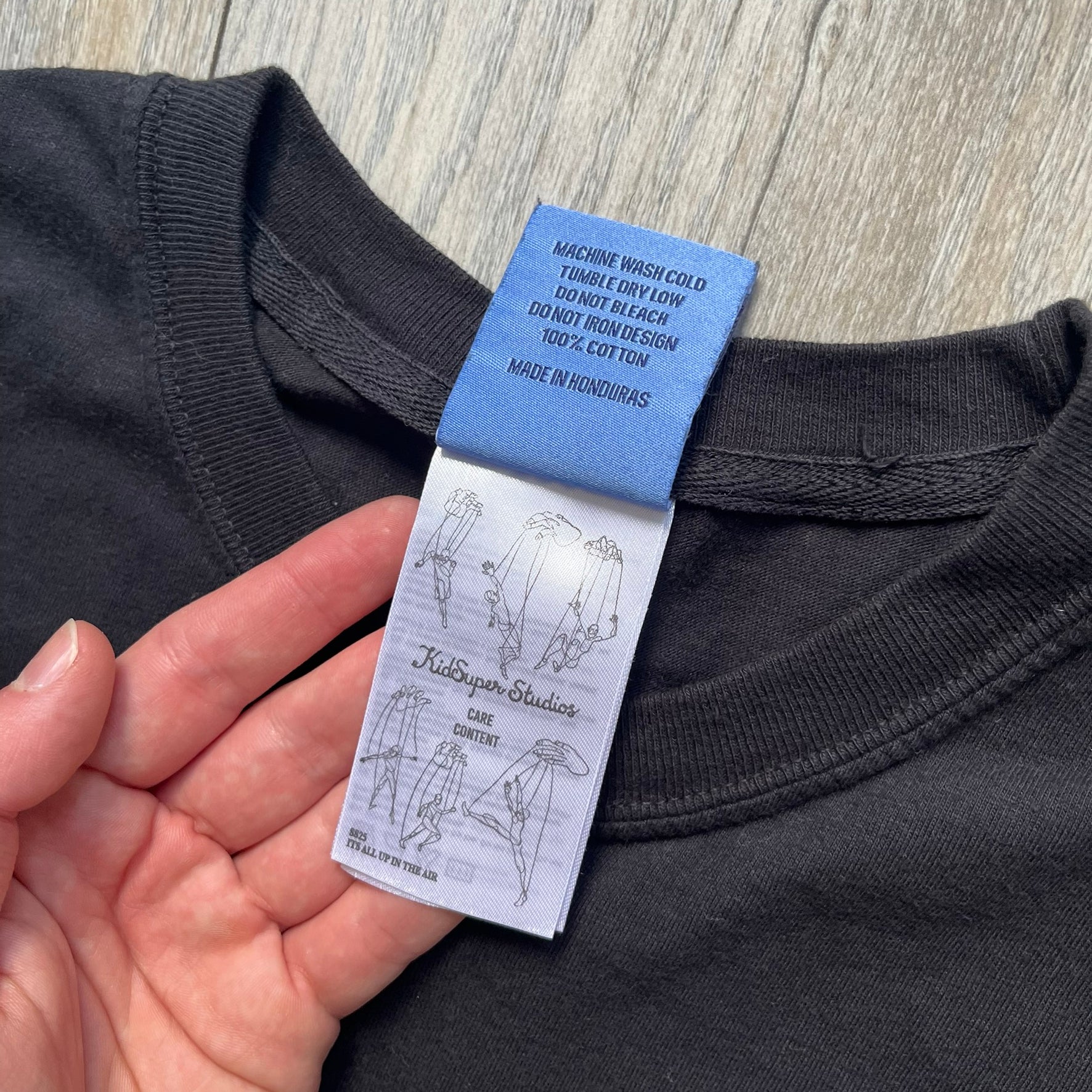 KidSuper Studios SS25 “Get Up, Get Goin’” Black Tee is a black short-sleeve T-shirt from the Spring/Summer 2025 collection. The front features a white and light blue graphic of a figure holding a briefcase mid-jump in a parkour-style pose above the “Kidsuper Studios Get Up, Get Goin’” text. The shirt includes a KidSuper SS25 blue neck tag.
