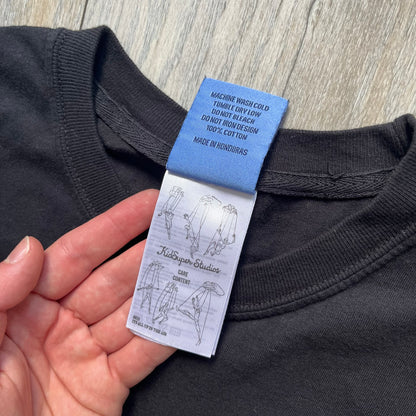 KidSuper Studios SS25 “Get Up, Get Goin’” Black Tee is a black short-sleeve T-shirt from the Spring/Summer 2025 collection. The front features a white and light blue graphic of a figure holding a briefcase mid-jump in a parkour-style pose above the “Kidsuper Studios Get Up, Get Goin’” text. The shirt includes a KidSuper SS25 blue neck tag.
