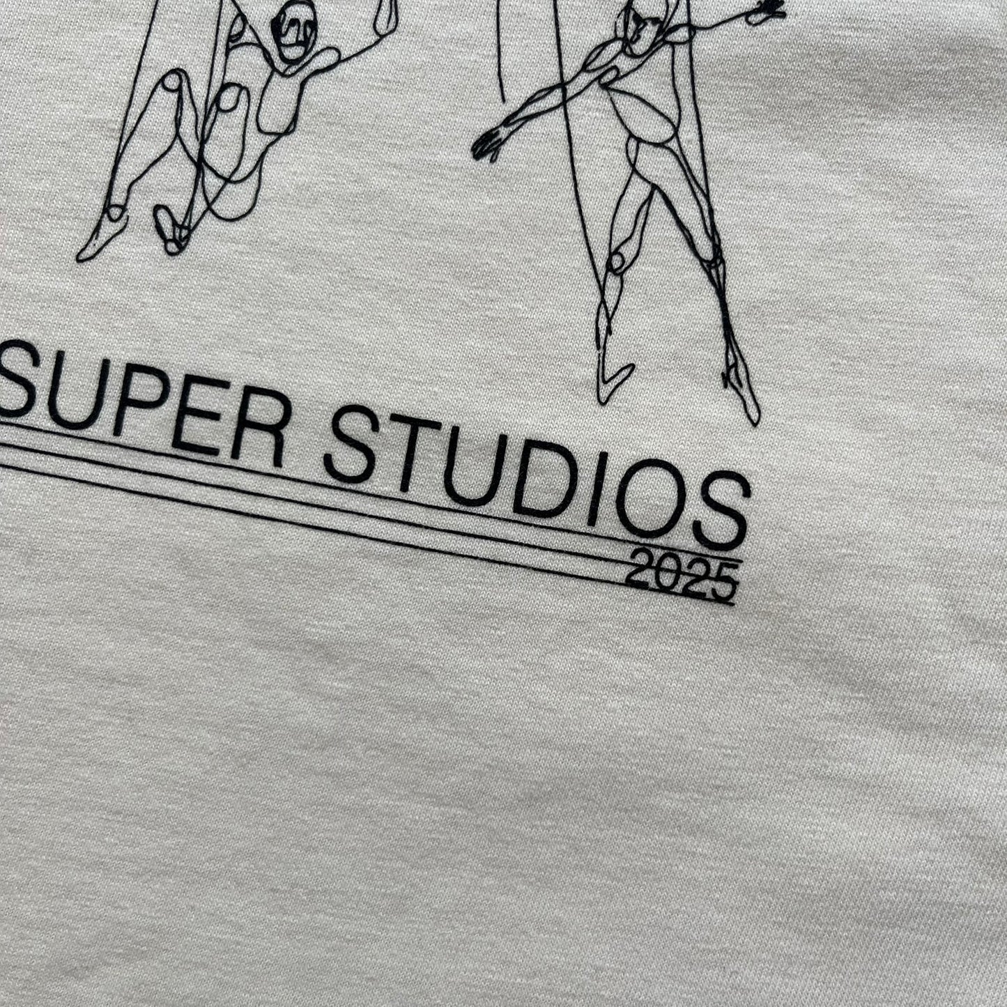 KidSuper Studios SS25 “String Puppets” Cream Tee is a cream short-sleeve T-shirt from the Spring/Summer 2025 collection. The front features five black string puppet-style figures on the chest, with “Kidsuper Studios 2025” text/logo printed underneath. The shirt includes a blue SS25 KidSuper neck tag.