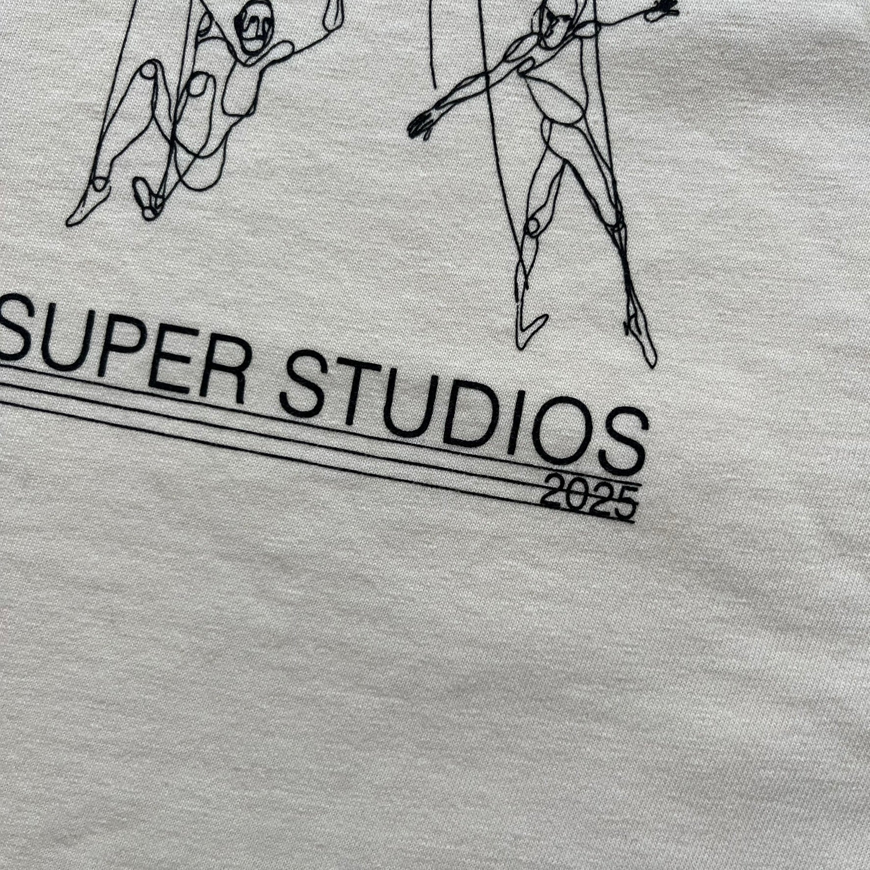 KidSuper Studios SS25 “String Puppets” Cream Tee is a cream short-sleeve T-shirt from the Spring/Summer 2025 collection. The front features five black string puppet-style figures on the chest, with “Kidsuper Studios 2025” text/logo printed underneath. The shirt includes a blue SS25 KidSuper neck tag.