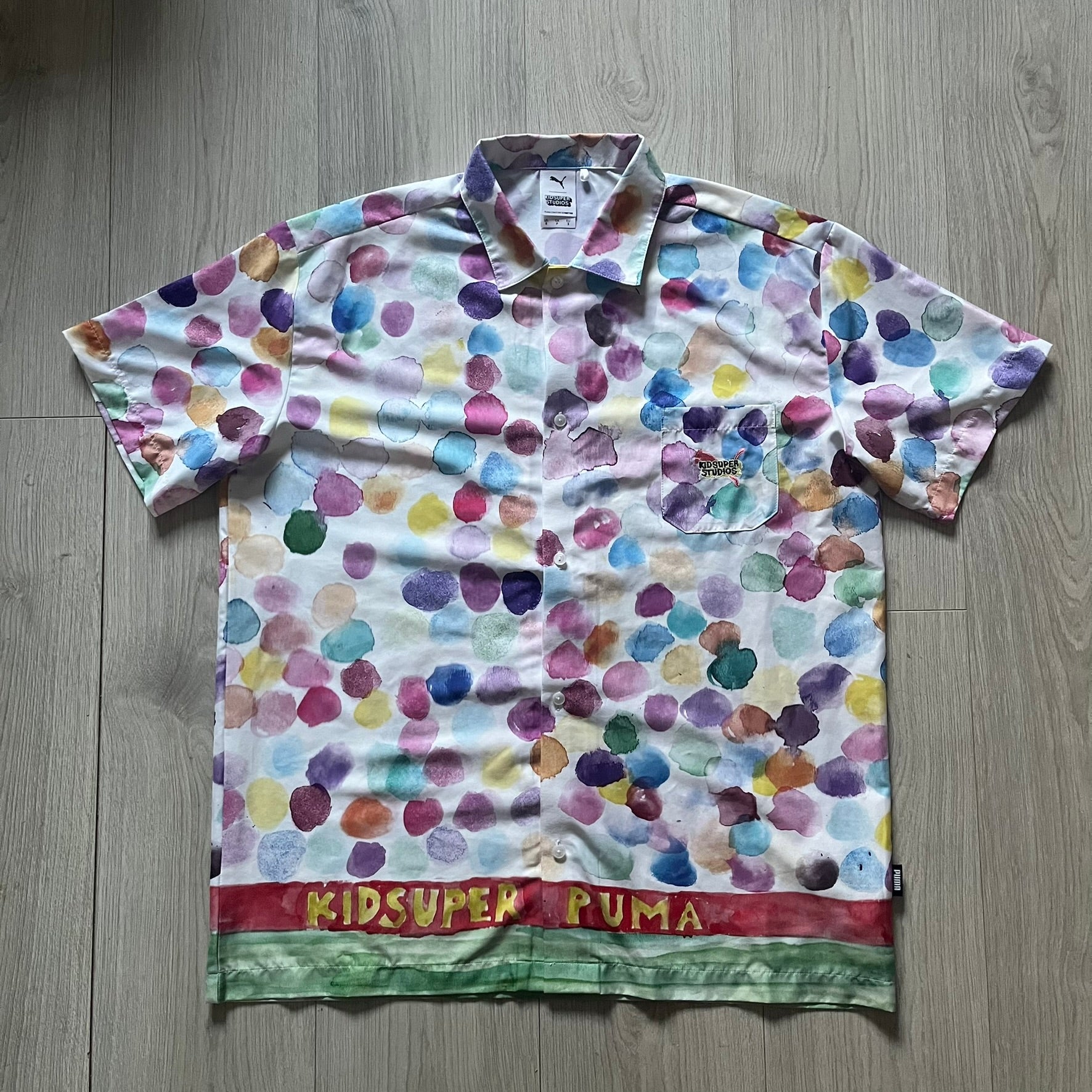 From the KidSuper Studios x Puma 2020 collection, this reversible football shirt (598953-02) showcases a watercolor-style all-over crowd print with vibrant color detailing. The design includes a red and yellow co-branded banner, a green field stripe and a back graphic of a football player doing a bicycle kick. Complete with a chest pocket and embroidered KidSuper Studios x Puma logo.