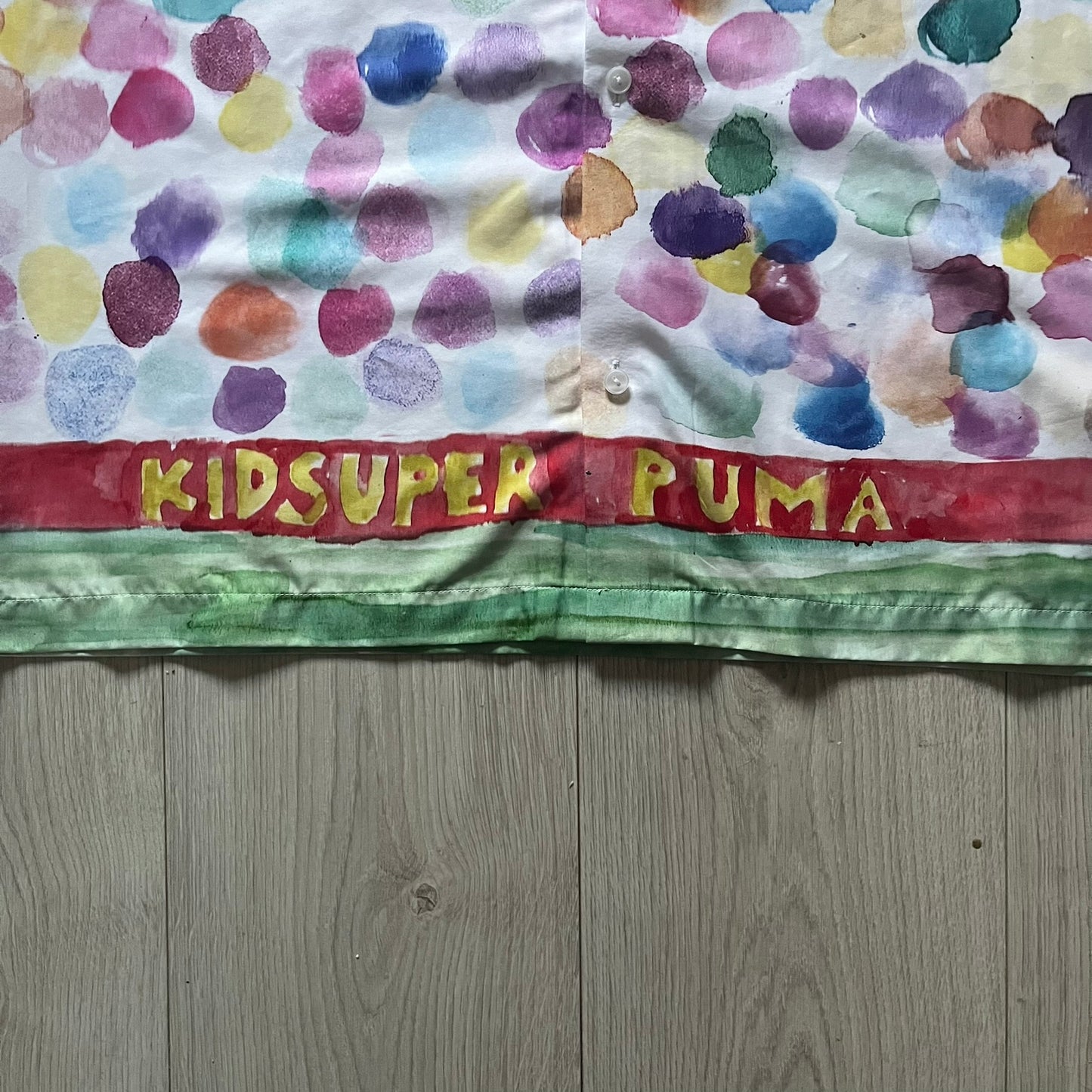 From the KidSuper Studios x Puma 2020 collection, this reversible football shirt (598953-02) showcases a watercolor-style all-over crowd print with vibrant color detailing. The design includes a red and yellow co-branded banner, a green field stripe and a back graphic of a football player doing a bicycle kick. Complete with a chest pocket and embroidered KidSuper Studios x Puma logo.