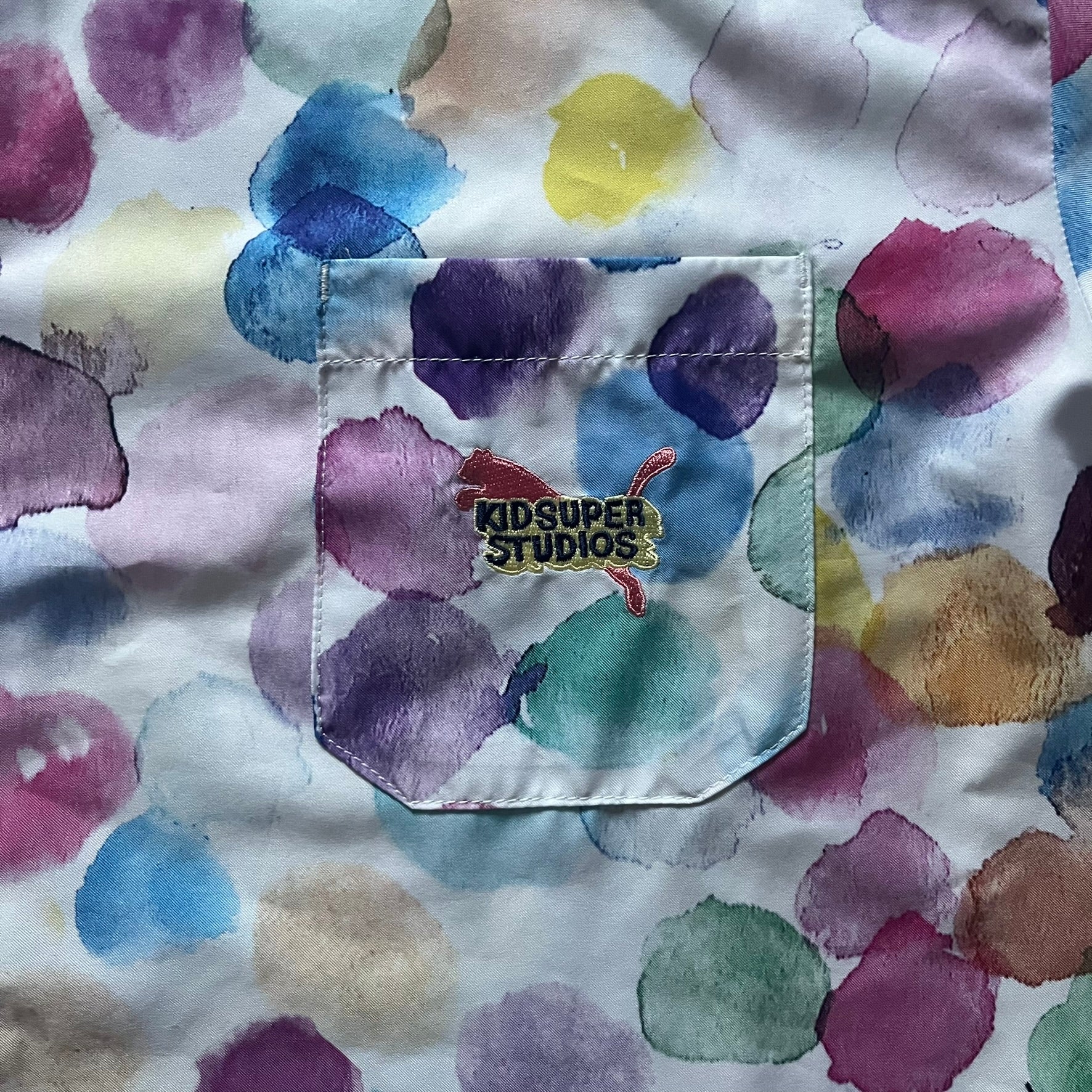 From the KidSuper Studios x Puma 2020 collection, this reversible football shirt (598953-02) showcases a watercolor-style all-over crowd print with vibrant color detailing. The design includes a red and yellow co-branded banner, a green field stripe and a back graphic of a football player doing a bicycle kick. Complete with a chest pocket and embroidered KidSuper Studios x Puma logo.