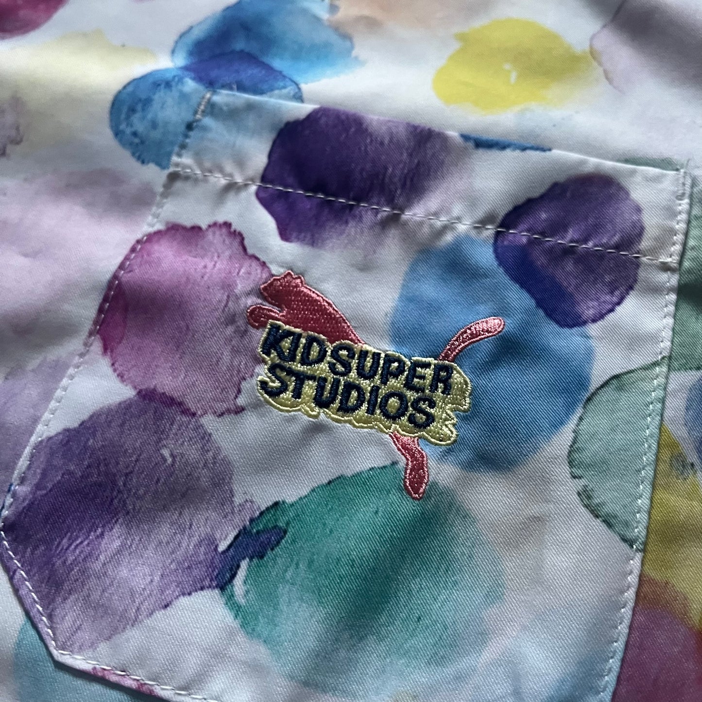 From the KidSuper Studios x Puma 2020 collection, this reversible football shirt (598953-02) showcases a watercolor-style all-over crowd print with vibrant color detailing. The design includes a red and yellow co-branded banner, a green field stripe and a back graphic of a football player doing a bicycle kick. Complete with a chest pocket and embroidered KidSuper Studios x Puma logo.