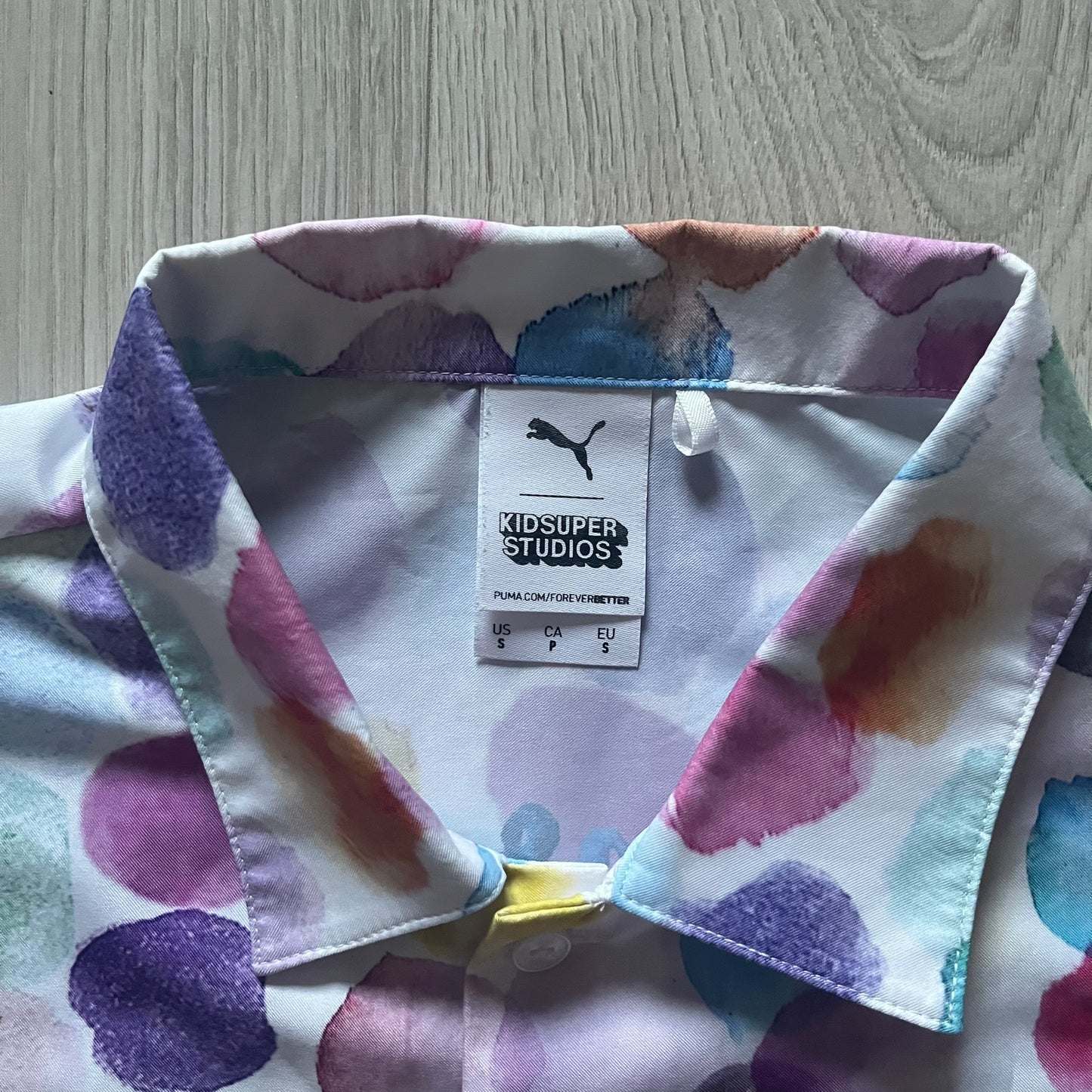 From the KidSuper Studios x Puma 2020 collection, this reversible football shirt (598953-02) showcases a watercolor-style all-over crowd print with vibrant color detailing. The design includes a red and yellow co-branded banner, a green field stripe and a back graphic of a football player doing a bicycle kick. Complete with a chest pocket and embroidered KidSuper Studios x Puma logo.