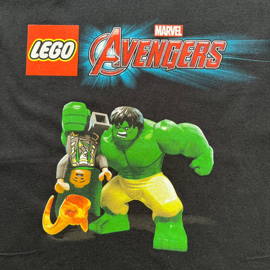 LEGO Avengers 2016 Promo Tee is a black T-shirt featuring a LEGO Marvel Avengers logo on the front. Below the logo is a graphic of LEGO Hulk holding Loki upside down. The shirt is made on a Gildan blank and includes 2016 LEGO and Marvel licensing inside the shirt.