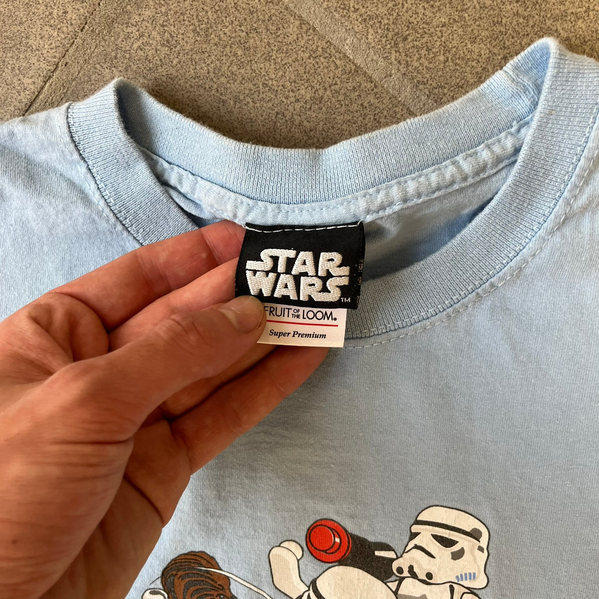 LEGO Star Wars 2007 “Let the WOOKIEE win!” Tee is a light blue, 100% cotton T-shirt with a front graphic of LEGO Chewbacca and two Stormtroopers, with Chewbacca holding the hands of one while the other stands to the side with a blaster. “Let the Wookiee win” text sits below the graphic, along with a small LEGO Star Wars logo and 2007 licensing. It has a Star Wars neck tag.