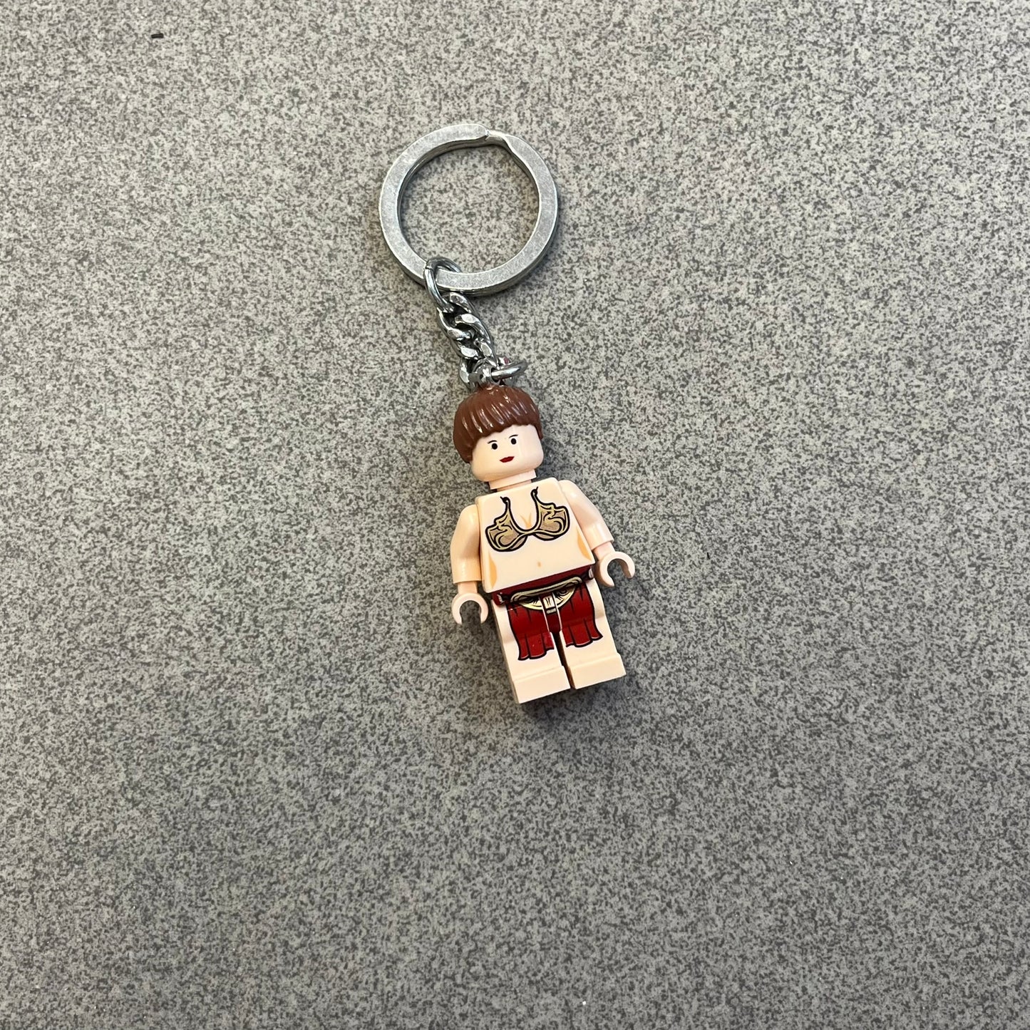 LEGO Star Wars 851938 Princess Leia Key Chain is a 2007 LEGO Gear accessory featuring a Princess Leia minifigure attached to a metal key ring and chain. The figure is permanently fixed to the chain and cannot be removed. The minifigure depicts Princess Leia in her bikini outfit from Jabba’s sail barge scene in Star Wars: Return of the Jedi.