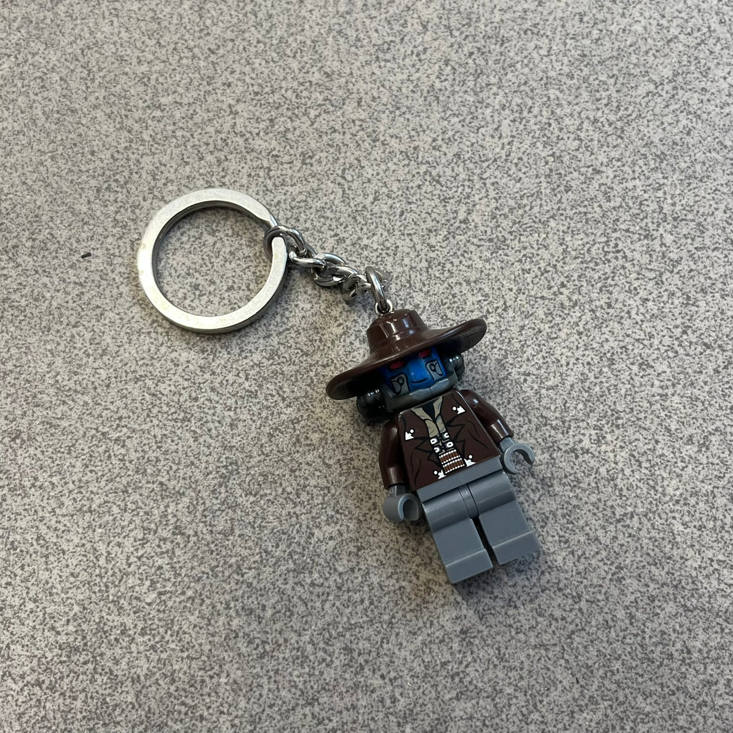 LEGO Star Wars 853127 Cad Bane Key Chain is a 2011 LEGO Gear accessory featuring a Cad Bane minifigure attached to a metal key ring and chain. The figure is permanently fixed to the chain and cannot be removed. The design depicts Cad Bane, the Duros bounty hunter from Star Wars: The Clone Wars, including his signature hat and outfit details.
