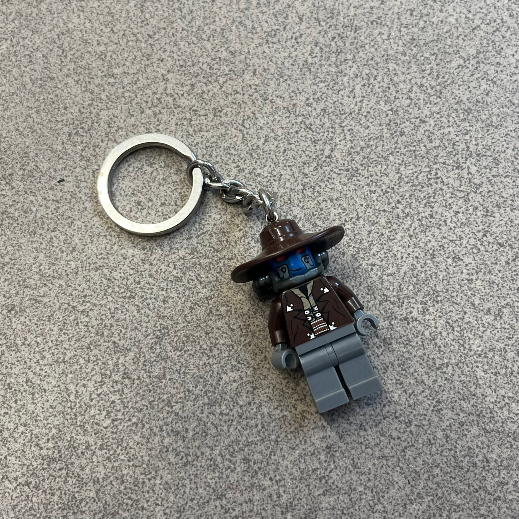 LEGO Star Wars 853127 Cad Bane Key Chain is a 2011 LEGO Gear accessory featuring a Cad Bane minifigure attached to a metal key ring and chain. The figure is permanently fixed to the chain and cannot be removed. The design depicts Cad Bane, the Duros bounty hunter from Star Wars: The Clone Wars, including his signature hat and outfit details.