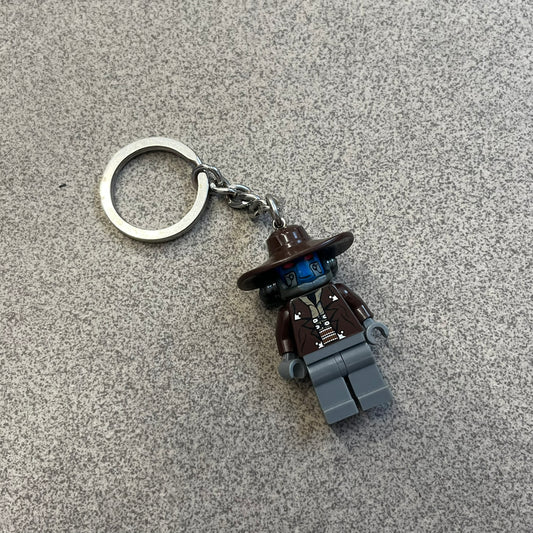 LEGO Star Wars 853127 Cad Bane Key Chain is a 2011 LEGO Gear accessory featuring a Cad Bane minifigure attached to a metal key ring and chain. The figure is permanently fixed to the chain and cannot be removed. The design depicts Cad Bane, the Duros bounty hunter from Star Wars: The Clone Wars, including his signature hat and outfit details.