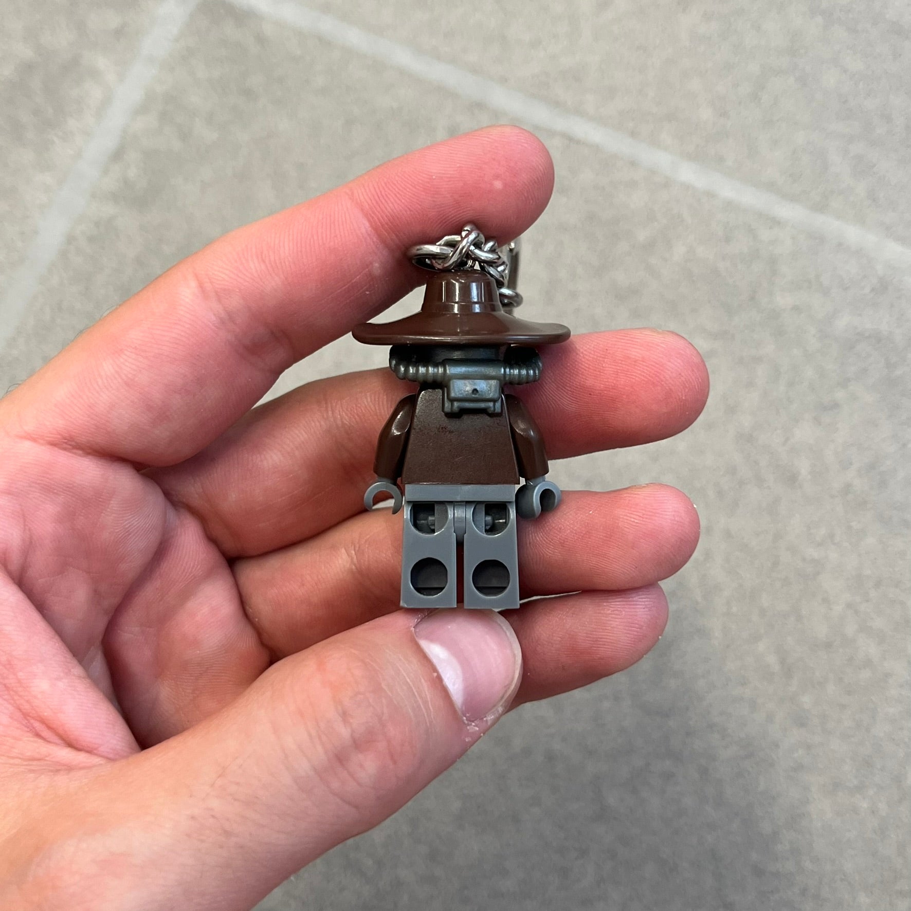 LEGO Star Wars 853127 Cad Bane Key Chain is a 2011 LEGO Gear accessory featuring a Cad Bane minifigure attached to a metal key ring and chain. The figure is permanently fixed to the chain and cannot be removed. The design depicts Cad Bane, the Duros bounty hunter from Star Wars: The Clone Wars, including his signature hat and outfit details.