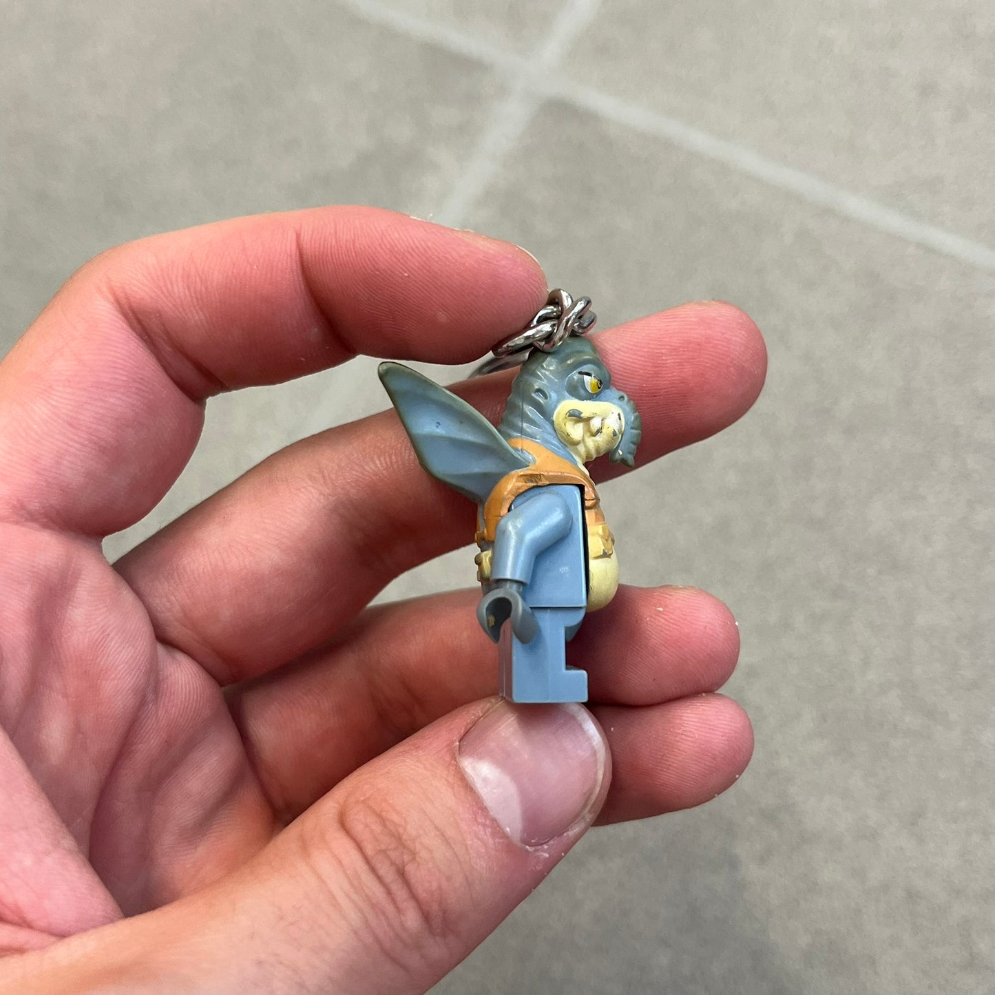 LEGO Star Wars 853413 Watto Key Chain is a 2012 LEGO Gear accessory featuring an authentic LEGO Watto minifigure attached to a metal key ring and chain. The Watto figure is permanently fixed to the chain and cannot be removed. The design represents Watto, the Toydarian junk dealer character from Star Wars: The Phantom Menace.