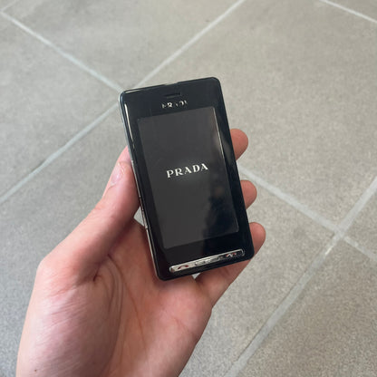 LG Prada KE850 Dummy Phone is a promotional display piece replicating the LG Prada KE850, the world's first capacitive touchscreen phone released through a collaboration between LG and Prada. It features the same black case, silver buttons, and top logo as the original, with a fake screen printed with the Prada logo, matching the real phone's size and design.