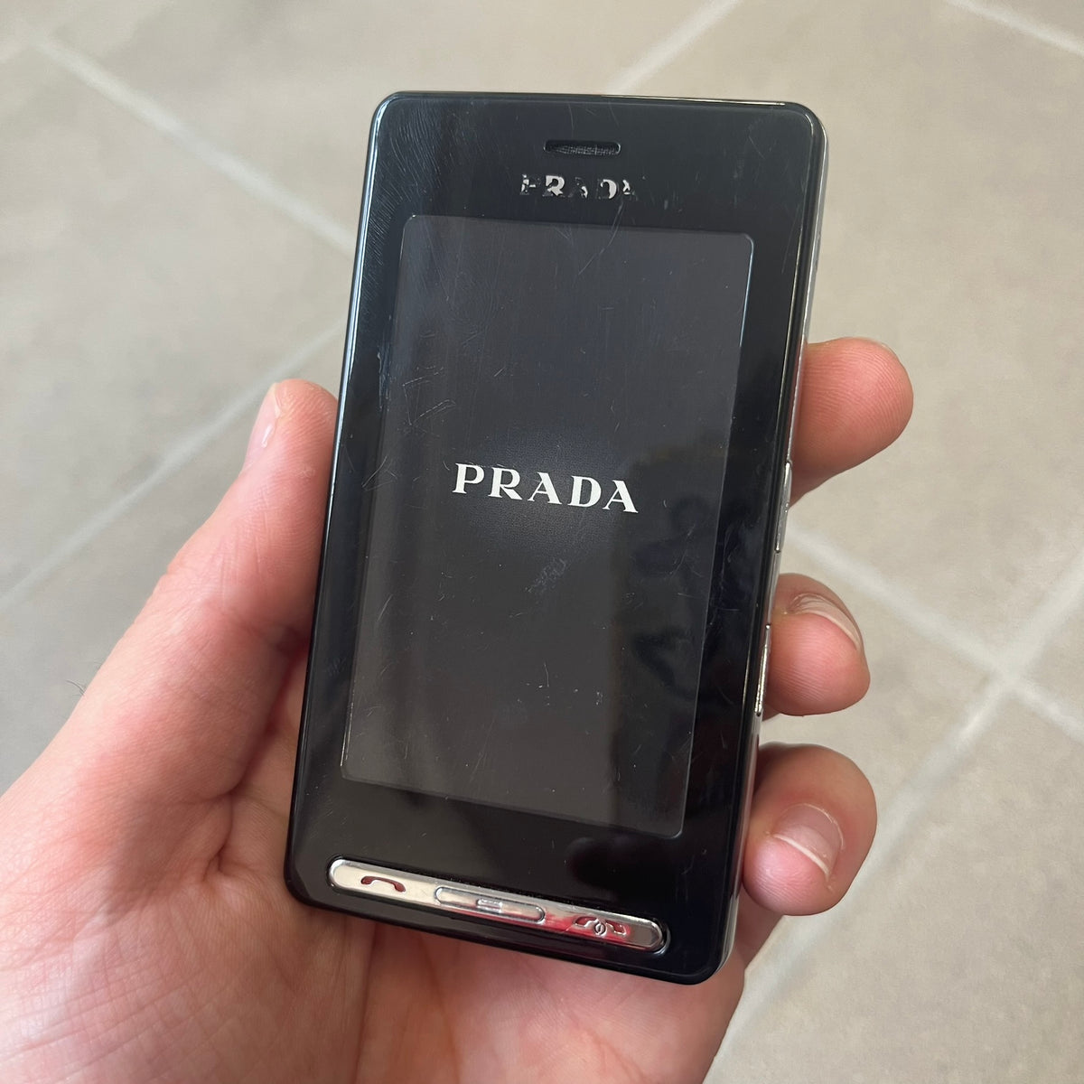 LG Prada KE850 Dummy Phone is a promotional display piece replicating the LG Prada KE850, the world's first capacitive touchscreen phone released through a collaboration between LG and Prada. It features the same black case, silver buttons, and top logo as the original, with a fake screen printed with the Prada logo, matching the real phone's size and design.