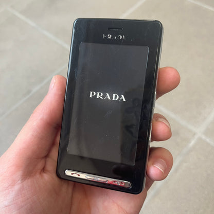 LG Prada KE850 Dummy Phone is a promotional display piece replicating the LG Prada KE850, the world's first capacitive touchscreen phone released through a collaboration between LG and Prada. It features the same black case, silver buttons, and top logo as the original, with a fake screen printed with the Prada logo, matching the real phone's size and design.