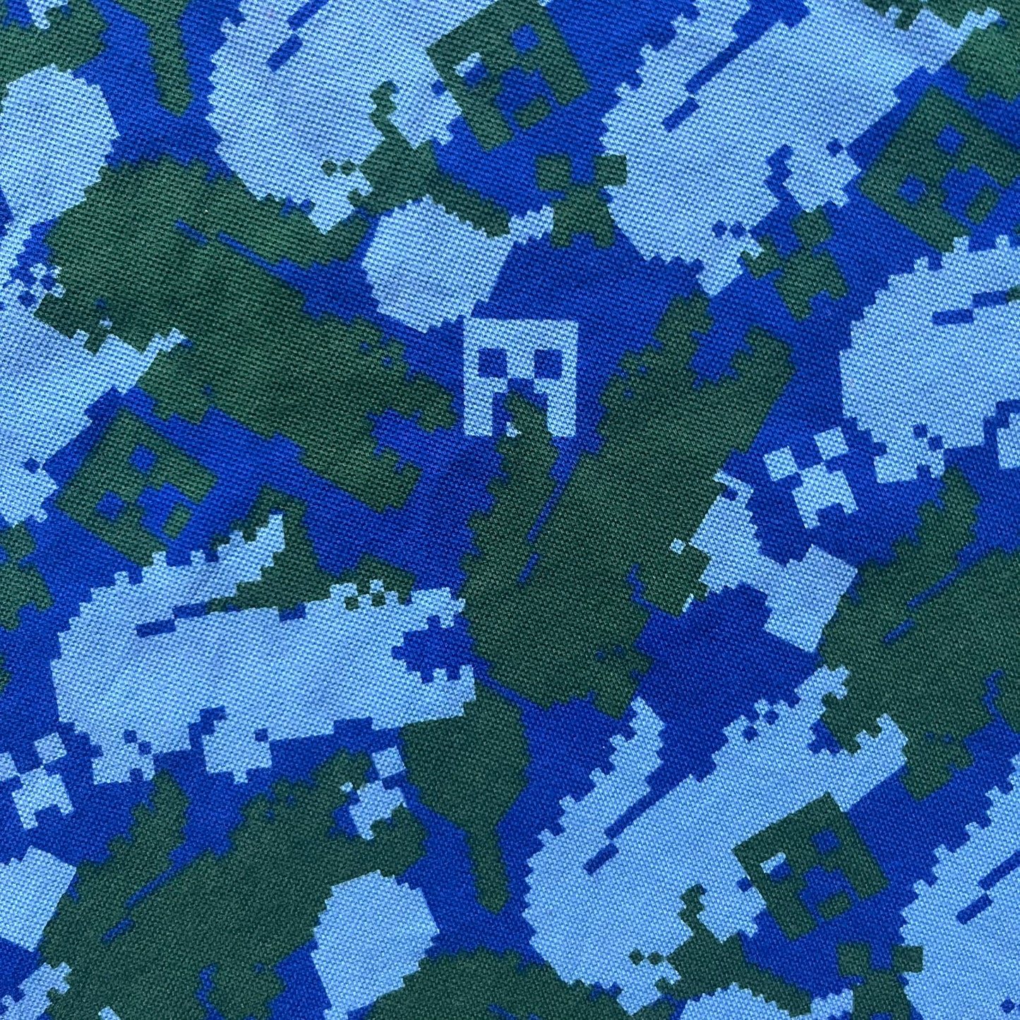 Blue short-sleeve polo shirt from the Lacoste x Minecraft collaboration, released as part of the Spring/Summer 2022 collection (drop in mid-March 2022). Features an all-over print of pixelated Lacoste crocodile logos in green and light blue, interspersed with Minecraft Creeper faces in matching tones. Designed with a solid ribbed polo collar, ribbed sleeve cuffs, and a two-button placket with square buttons featuring Minecraft branding. Finished with a Minecraft badge and a silicone Lacoste crocodile logo p