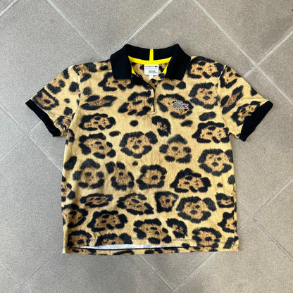 Lacoste x National Geographic AW20 Leopard Polo features an all-over beige, brown and black leopard print pattern across the fabric. The polo has black collar and sleeve hems, with a chest patch featuring the Lacoste crocodile logo in matching pattern colors.