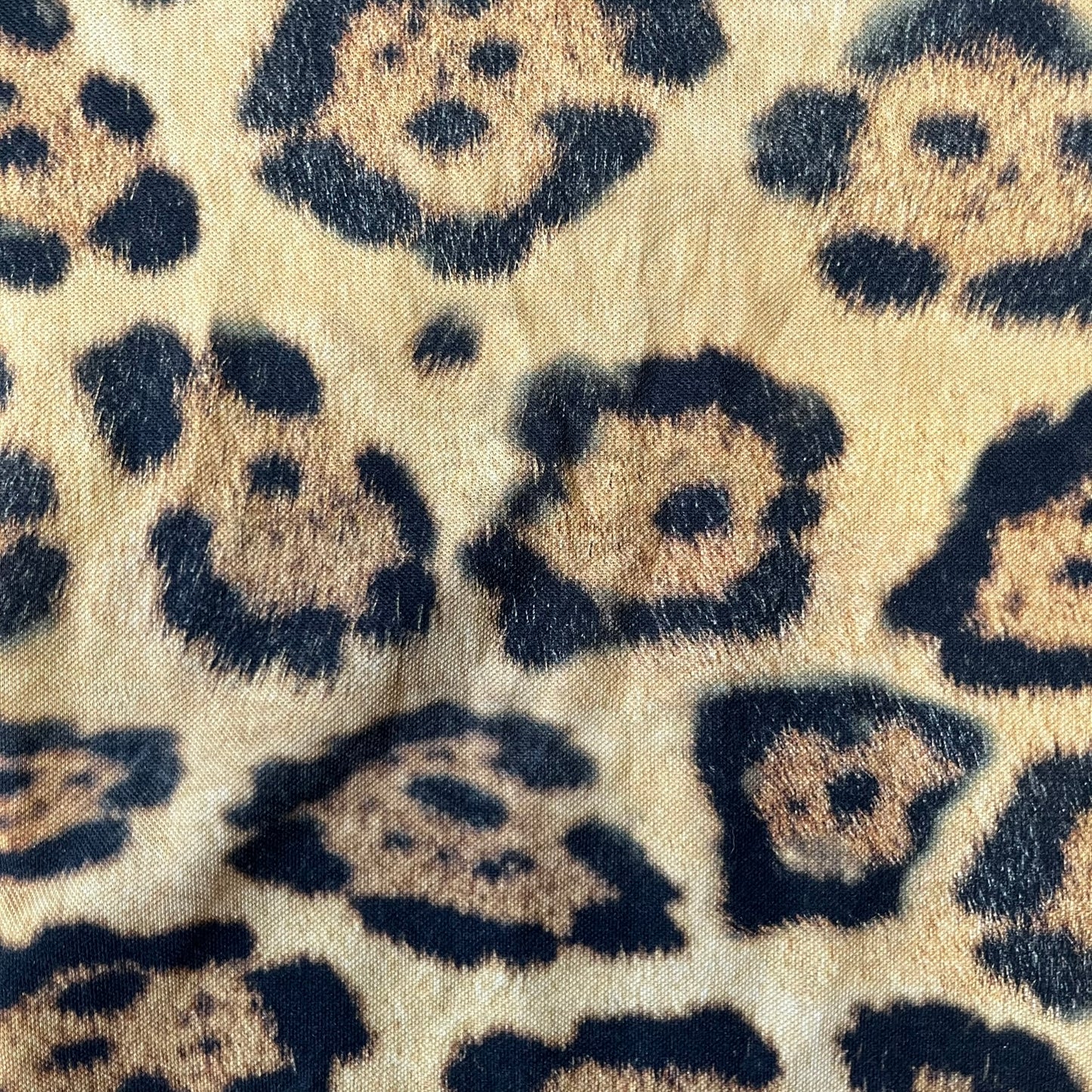 Lacoste x National Geographic AW20 Leopard Polo features an all-over beige, brown and black leopard print pattern across the fabric. The polo has black collar and sleeve hems, with a chest patch featuring the Lacoste crocodile logo in matching pattern colors.