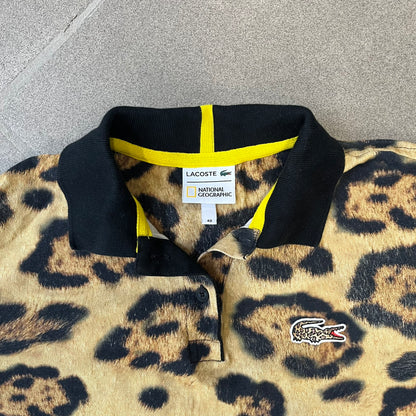 Lacoste x National Geographic AW20 Leopard Polo features an all-over beige, brown and black leopard print pattern across the fabric. The polo has black collar and sleeve hems, with a chest patch featuring the Lacoste crocodile logo in matching pattern colors.