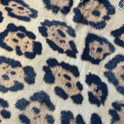 Lacoste x National Geographic AW20 Leopard Polo features an all-over beige, brown and black leopard print pattern across the fabric. The polo has beige collar and sleeve hems, with a chest patch featuring the Lacoste crocodile logo in matching pattern colors.