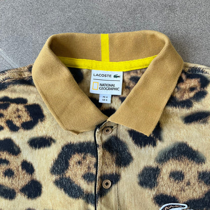 Lacoste x National Geographic AW20 Leopard Polo features an all-over beige, brown and black leopard print pattern across the fabric. The polo has beige collar and sleeve hems, with a chest patch featuring the Lacoste crocodile logo in matching pattern colors.