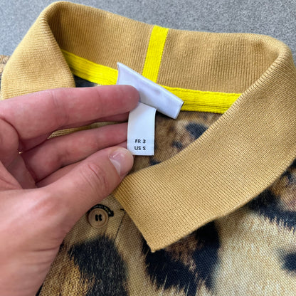 Lacoste x National Geographic AW20 Leopard Polo features an all-over beige, brown and black leopard print pattern across the fabric. The polo has beige collar and sleeve hems, with a chest patch featuring the Lacoste crocodile logo in matching pattern colors.