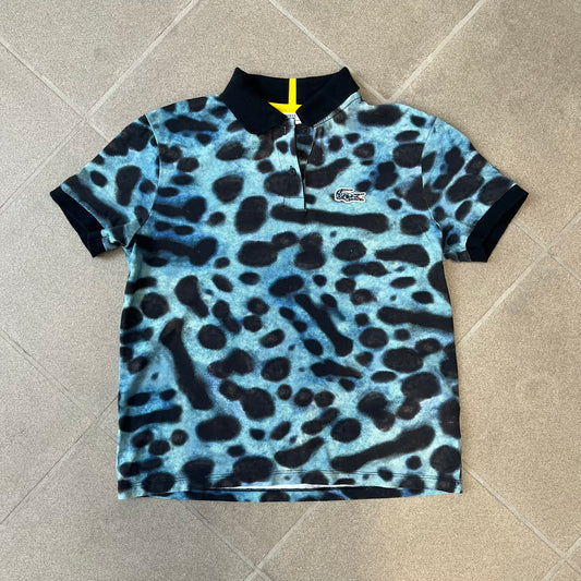 Lacoste x National Geographic AW20 Poison Dart Frog Polo features an all-over blue and black poison dart frog pattern across the fabric. The polo has black collar and sleeve hems, with a chest patch featuring the Lacoste crocodile logo in matching pattern colors.
