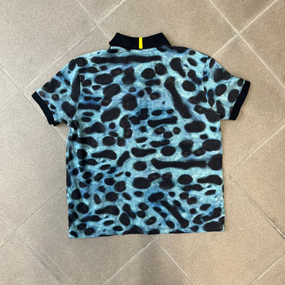 Lacoste x National Geographic AW20 Poison Dart Frog Polo features an all-over blue and black poison dart frog pattern across the fabric. The polo has black collar and sleeve hems, with a chest patch featuring the Lacoste crocodile logo in matching pattern colors.
