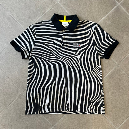  Lacoste x National Geographic AW20 Zebra Polo features an all-over white and black zebra print pattern across the fabric. The polo has black collar and sleeve hems, with a chest patch featuring the Lacoste crocodile logo in matching pattern colors.