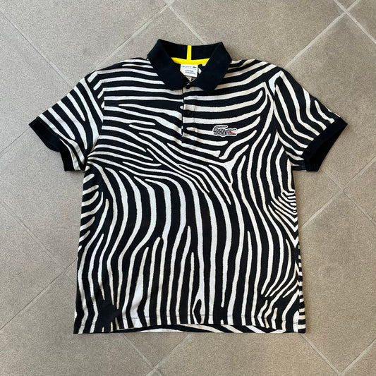  Lacoste x National Geographic AW20 Zebra Polo features an all-over white and black zebra print pattern across the fabric. The polo has black collar and sleeve hems, with a chest patch featuring the Lacoste crocodile logo in matching pattern colors.