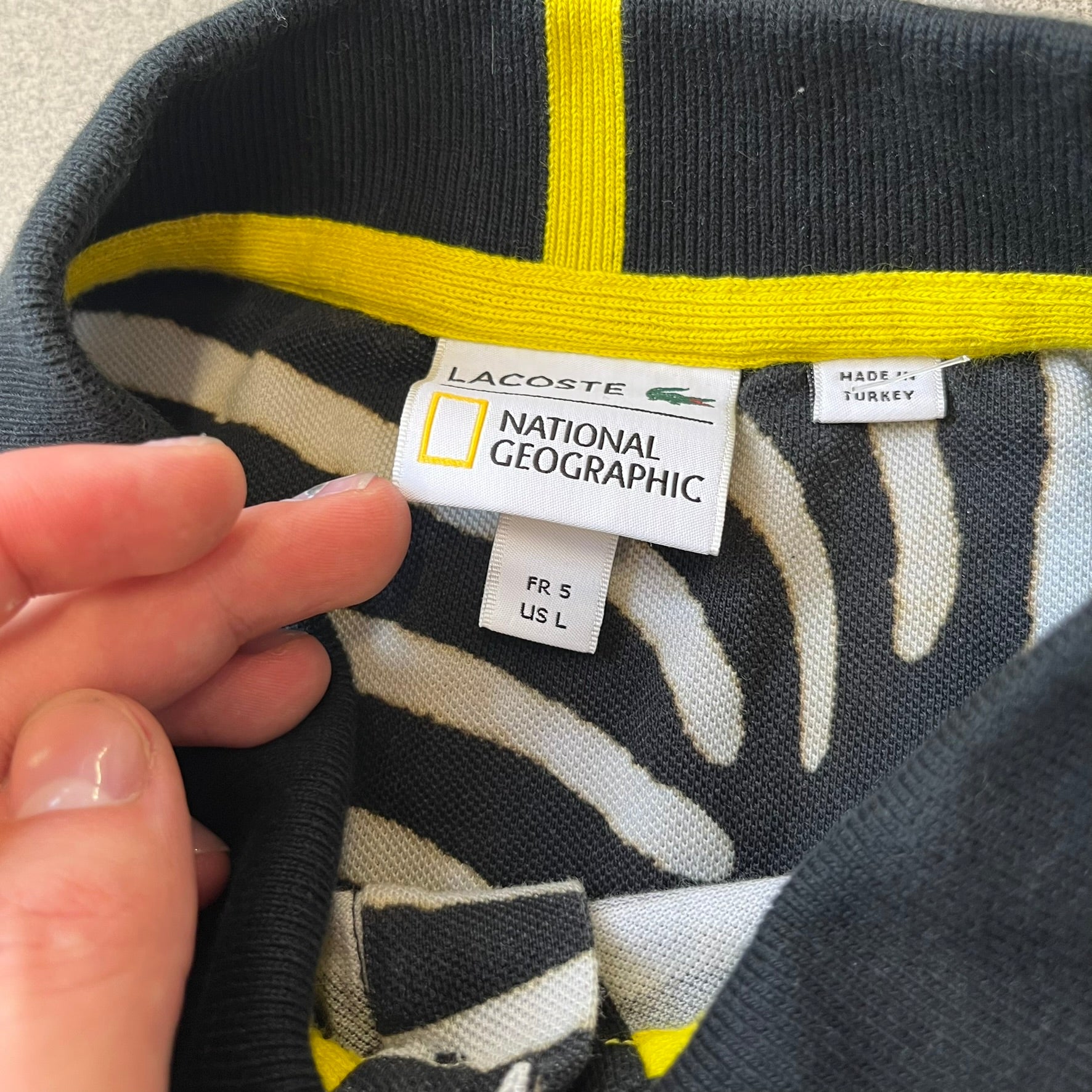  Lacoste x National Geographic AW20 Zebra Polo features an all-over white and black zebra print pattern across the fabric. The polo has black collar and sleeve hems, with a chest patch featuring the Lacoste crocodile logo in matching pattern colors.