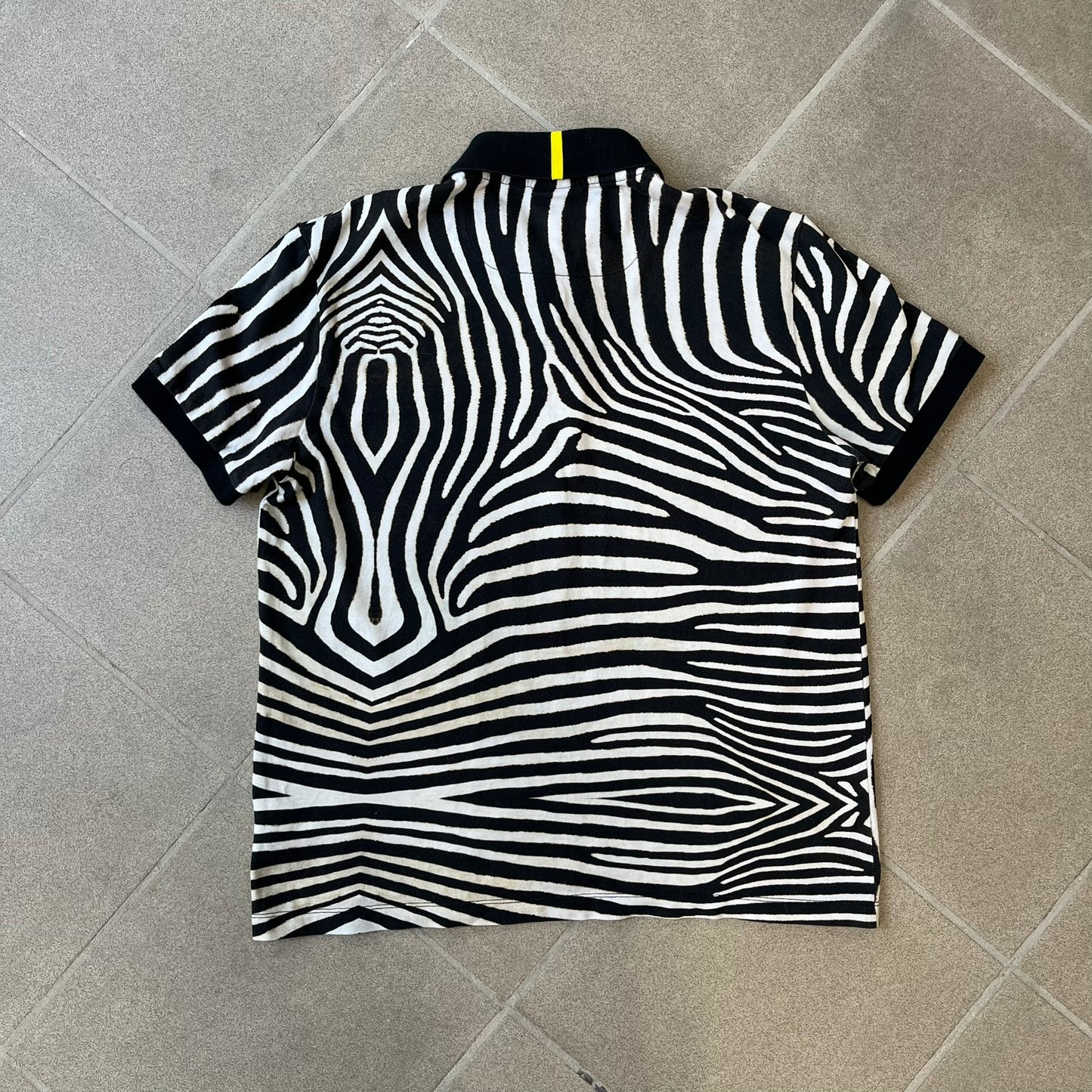  Lacoste x National Geographic AW20 Zebra Polo features an all-over white and black zebra print pattern across the fabric. The polo has black collar and sleeve hems, with a chest patch featuring the Lacoste crocodile logo in matching pattern colors.