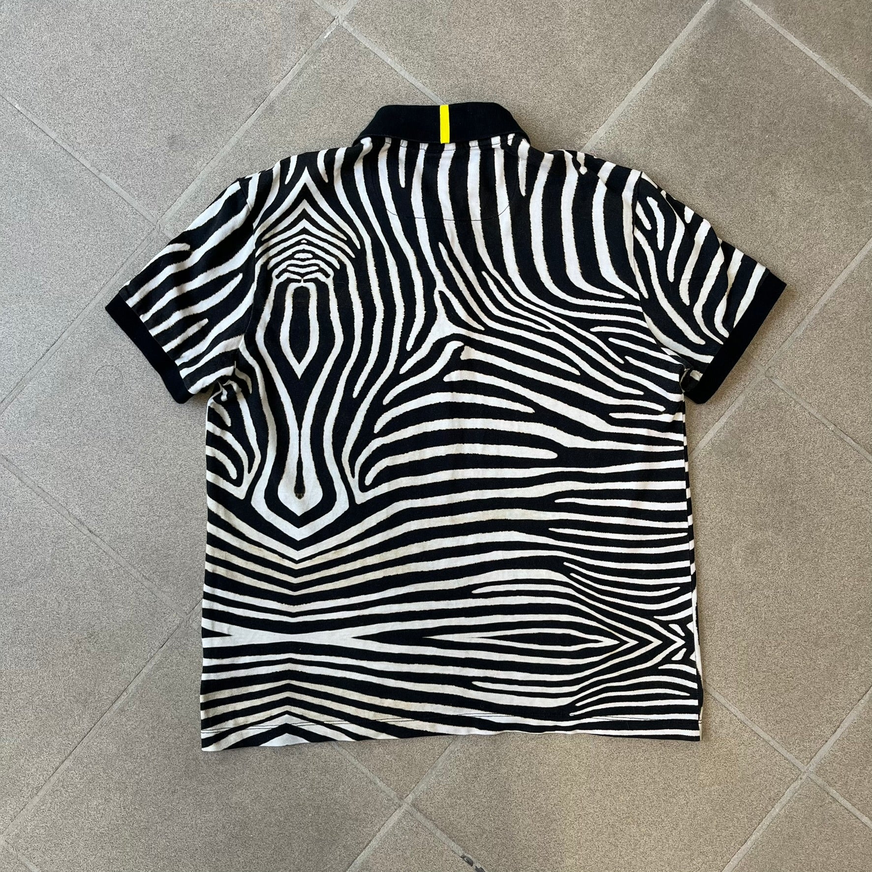  Lacoste x National Geographic AW20 Zebra Polo features an all-over white and black zebra print pattern across the fabric. The polo has black collar and sleeve hems, with a chest patch featuring the Lacoste crocodile logo in matching pattern colors.