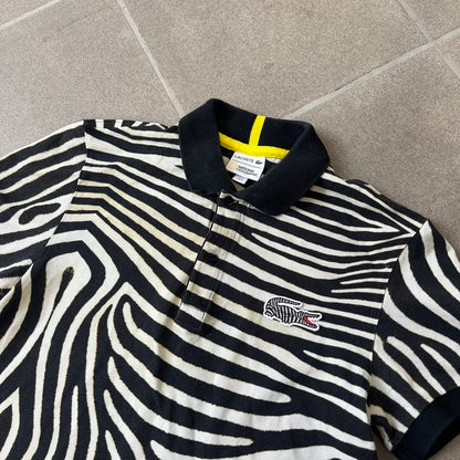 Lacoste x National Geographic AW20 Zebra Polo features an all-over white and black zebra print pattern across the fabric. The polo has black collar and sleeve hems, with a chest patch featuring the Lacoste crocodile logo in matching pattern colors.
