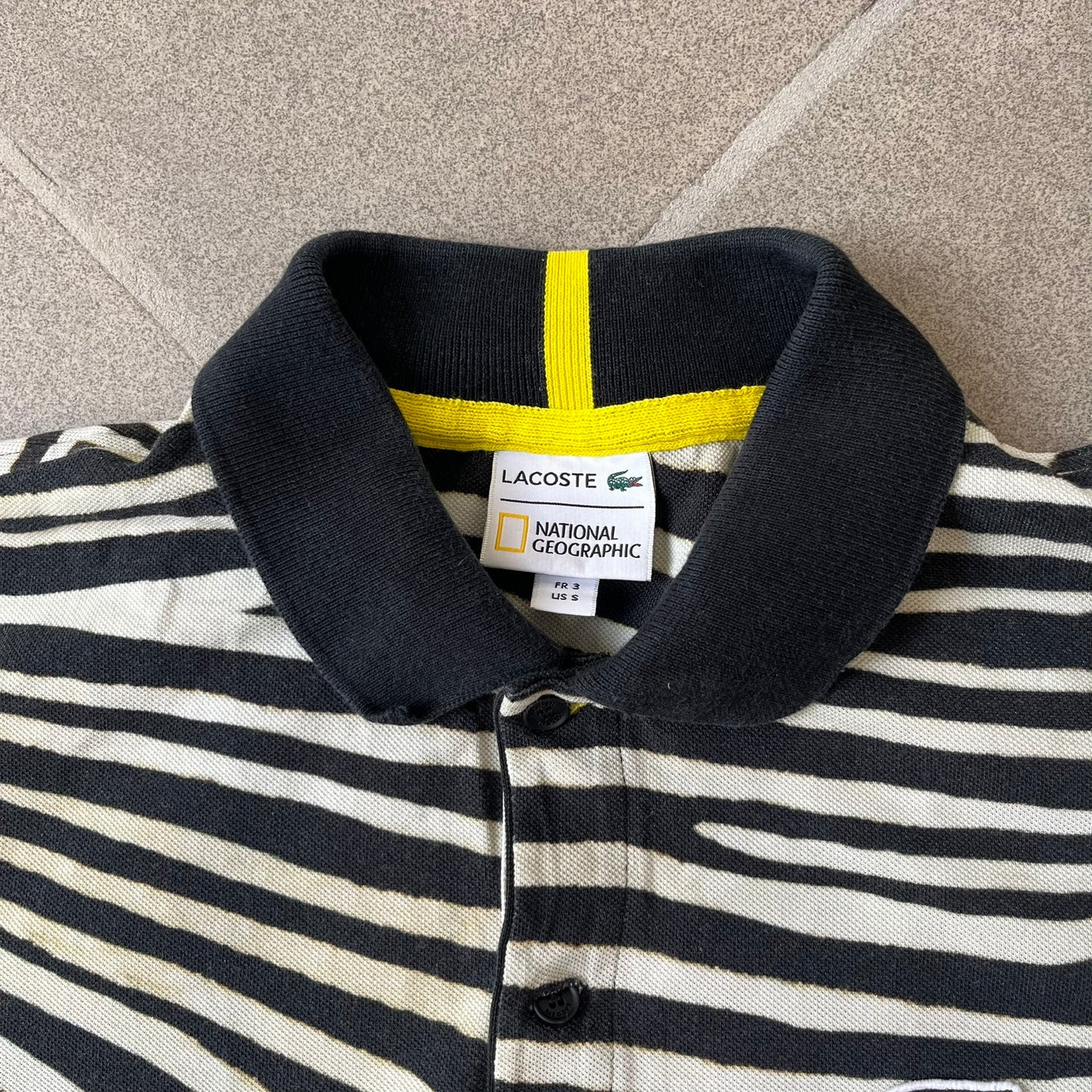 Lacoste x National Geographic AW20 Zebra Polo features an all-over white and black zebra print pattern across the fabric. The polo has black collar and sleeve hems, with a chest patch featuring the Lacoste crocodile logo in matching pattern colors.
