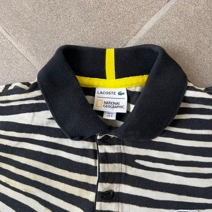 Lacoste x National Geographic AW20 Zebra Polo features an all-over white and black zebra print pattern across the fabric. The polo has black collar and sleeve hems, with a chest patch featuring the Lacoste crocodile logo in matching pattern colors.